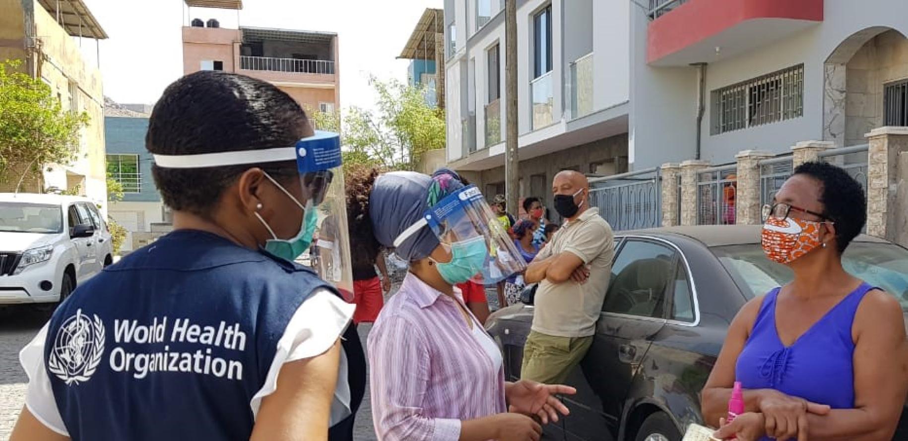 موظف في منظمة الصحة العالمية يقف مع امرأتين خارج أحد الأحياء في كابو فيردي.