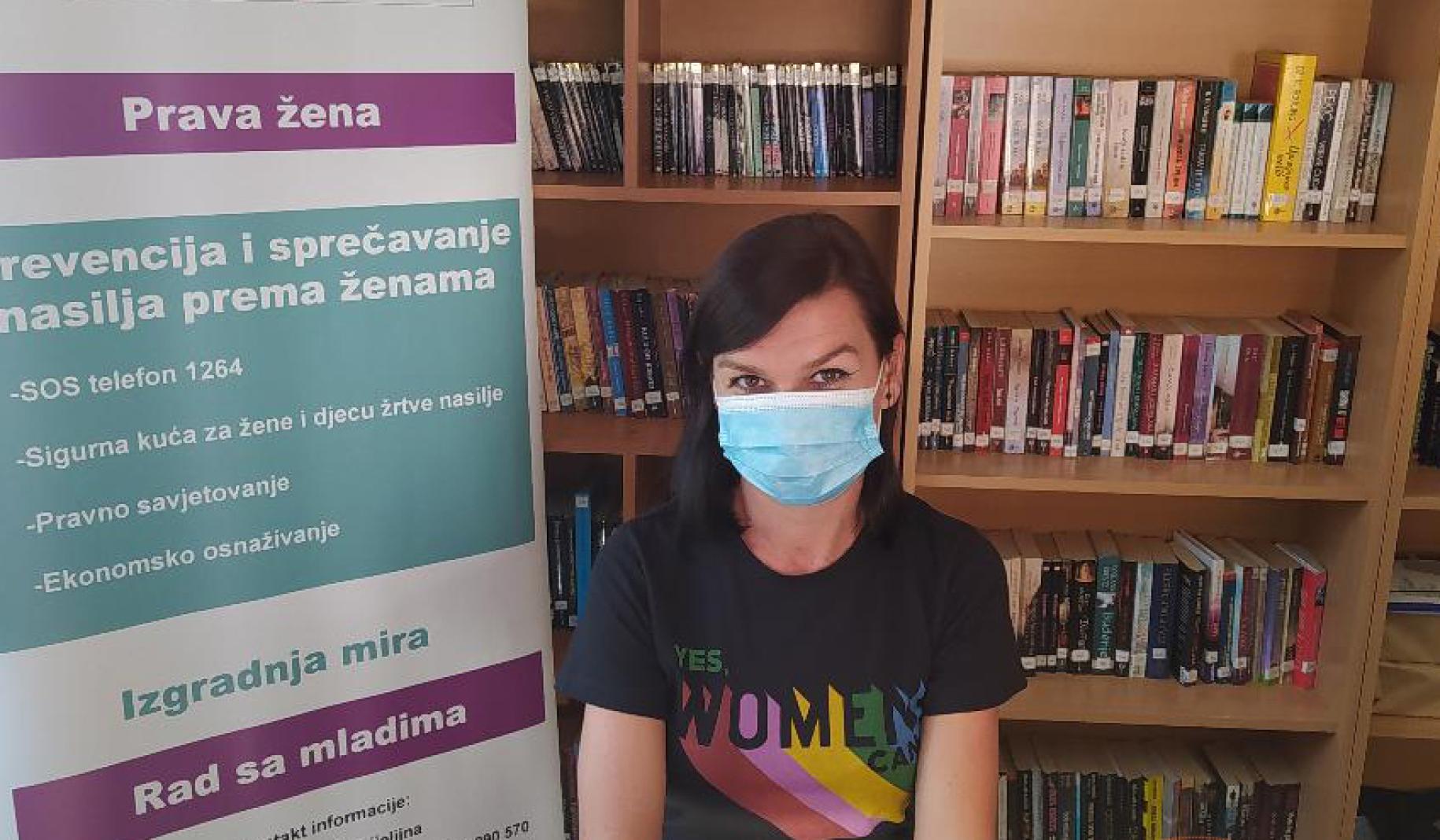 Dragana Petric se sienta frente a una estantería de libros y una señalización en la Fundación Lara Bijeljina.