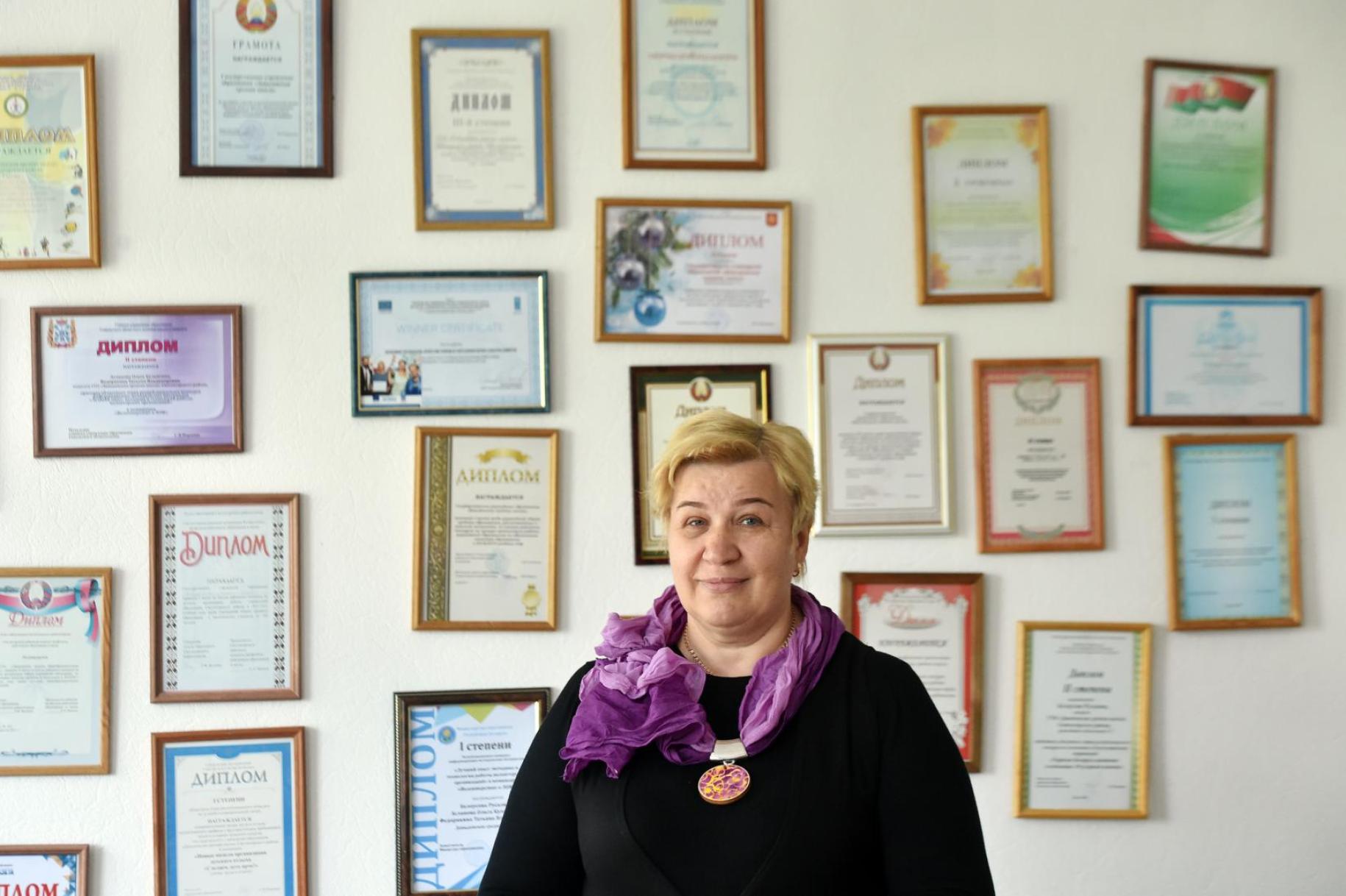 Svetlana Markevich, directora de la Escuela Secundaria Davydovskaya, está orgullosa frente a una pared de certificados y diplomas enmarcados.