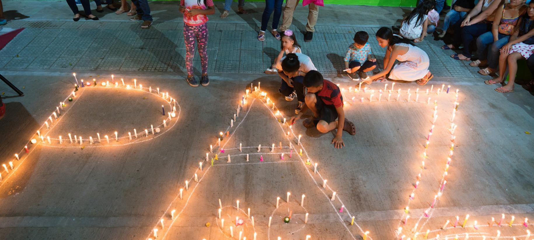Mujeres y niños encienden velas que forman la palabra paz, en Mocoa, Colombia.
