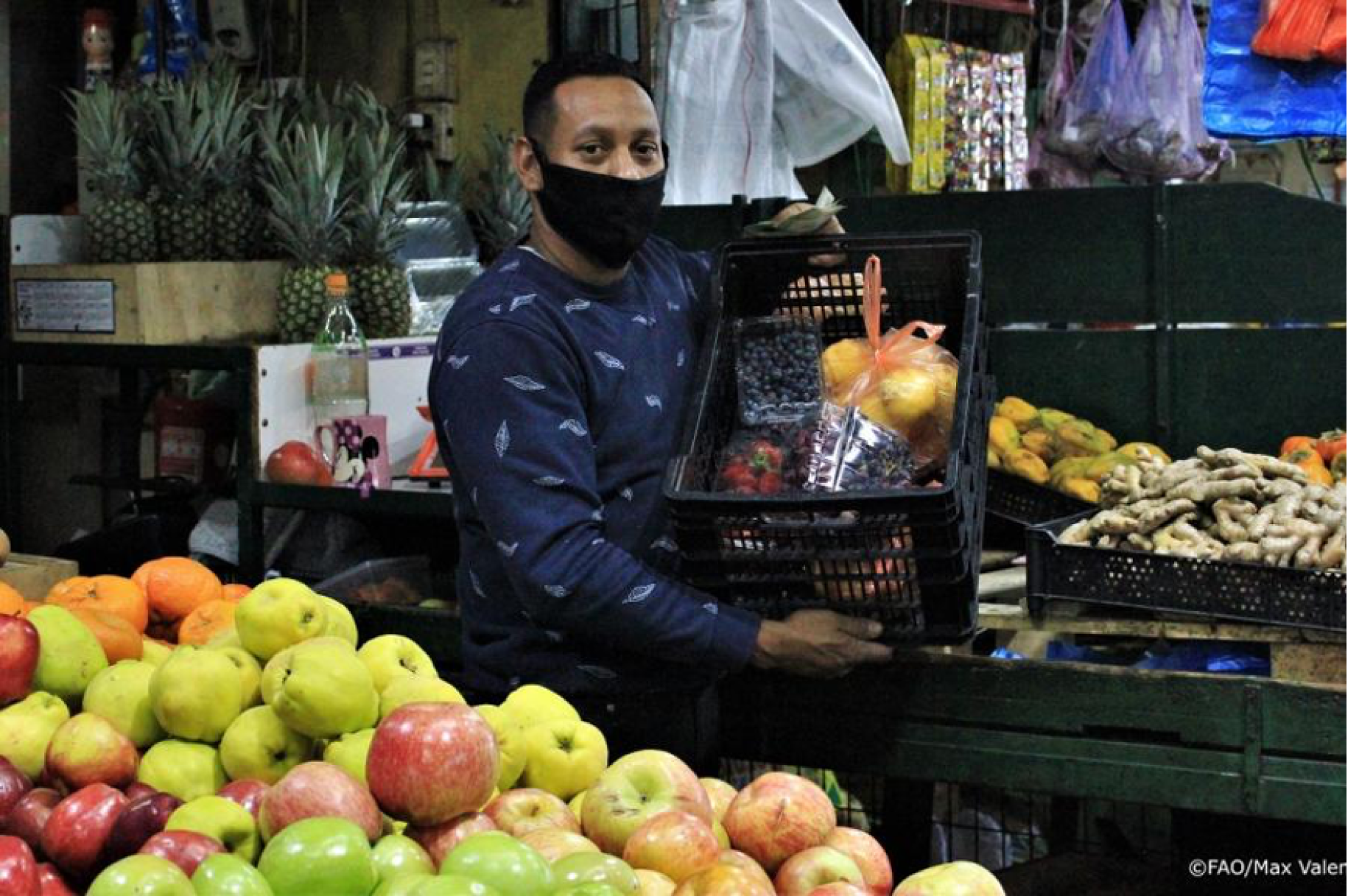 A man holds up a crate of of fruits and vegetables at a local food vendor.