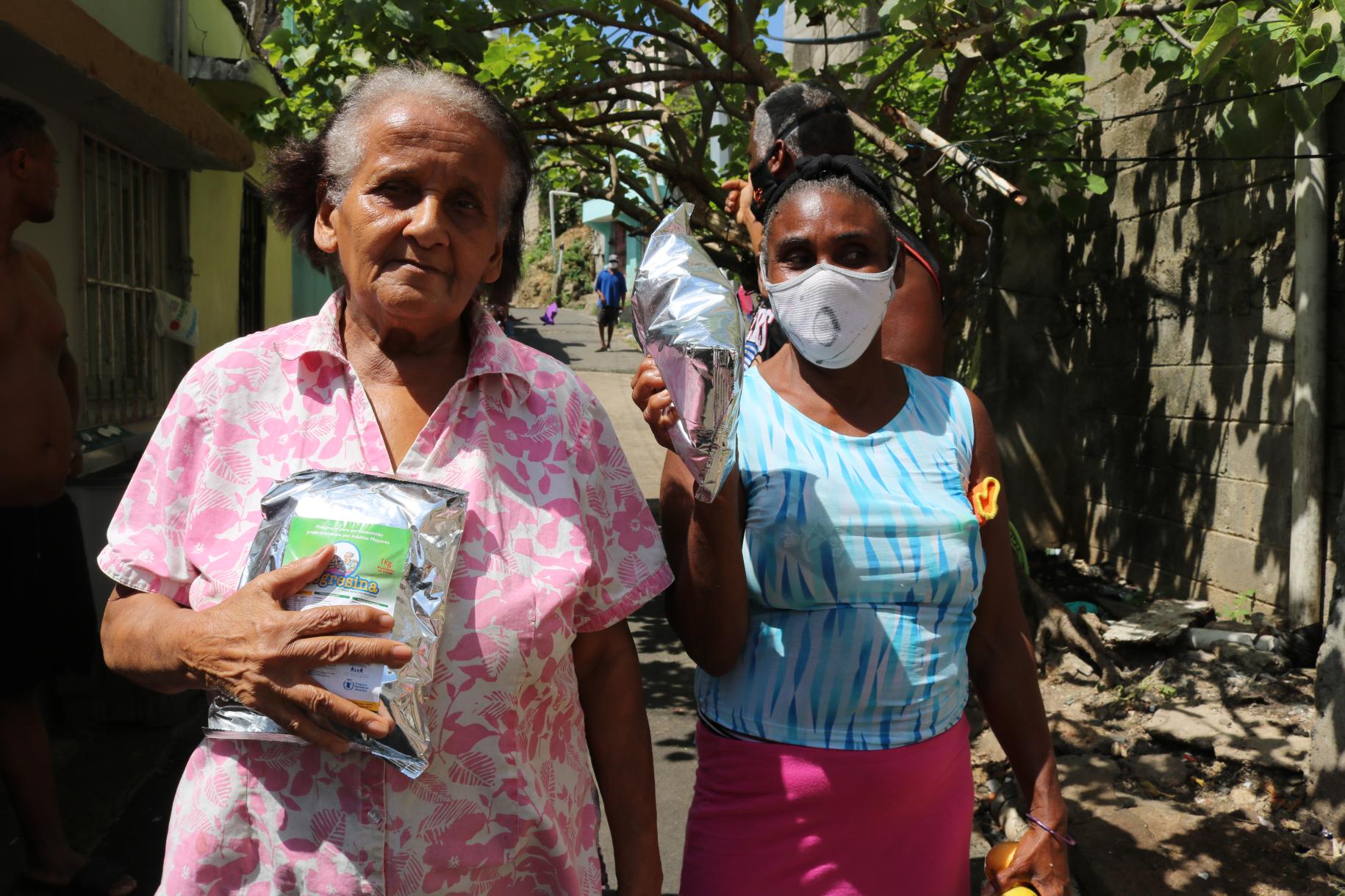 Two women prominently hold the food supplies received from the World Food Programme.