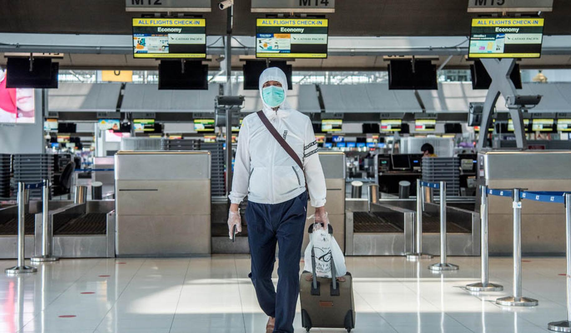 رجل يرتدي قناعا يمشي مع أمتعته في مطار سوفارنابومي، بانكوك، تايلاند.