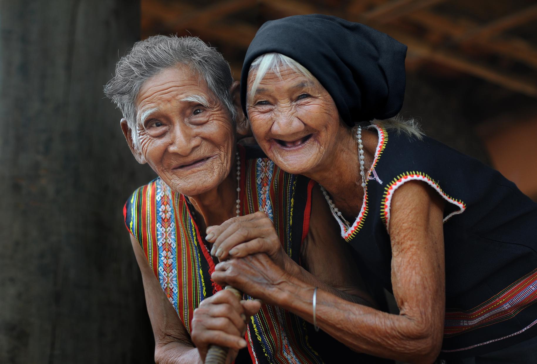 Dos risueñas mujeres mayores miran con alegría a la cámara. 
