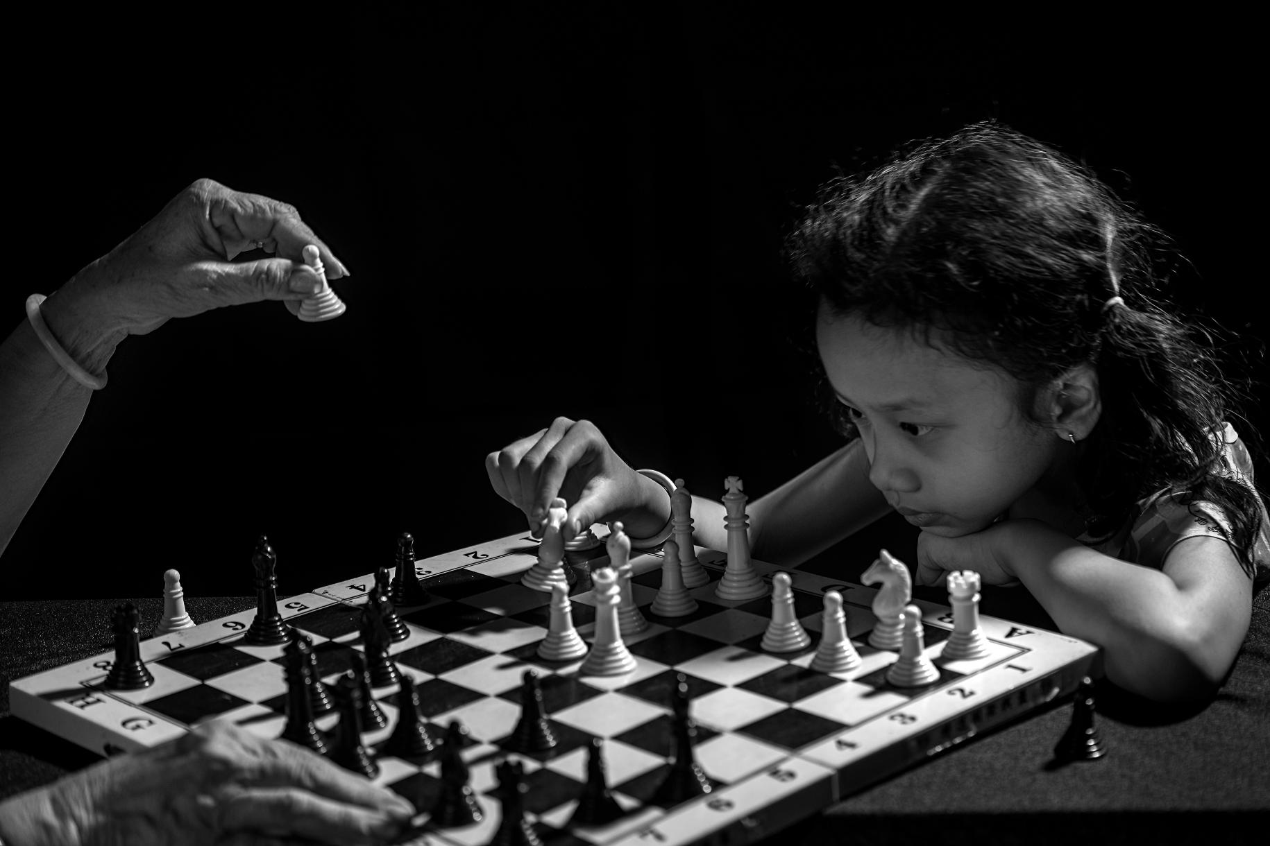 صورة بالأبيض والأسود لفتاة صغيرة تفكر بخطوتها التالية في لعبة الشطرنج مع جدتها.