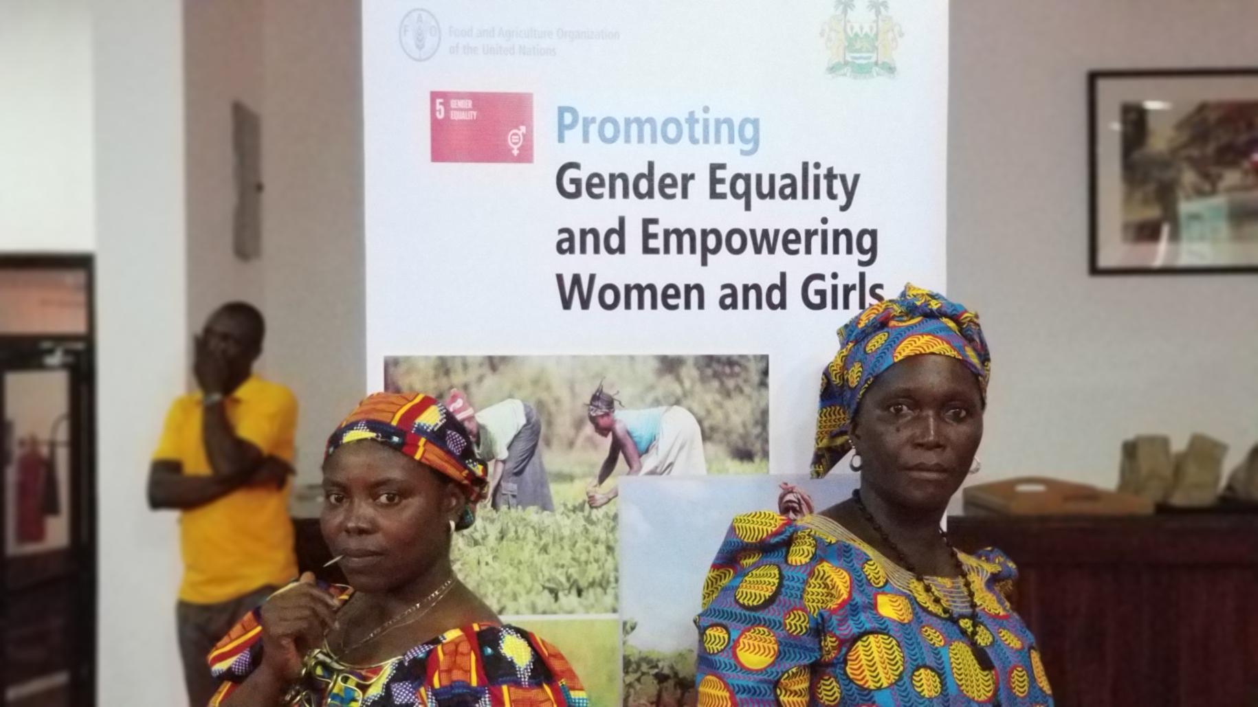 Two women stand powerfully in front of an banner promoting SDG 5: Gender equality and empowering women and girls.