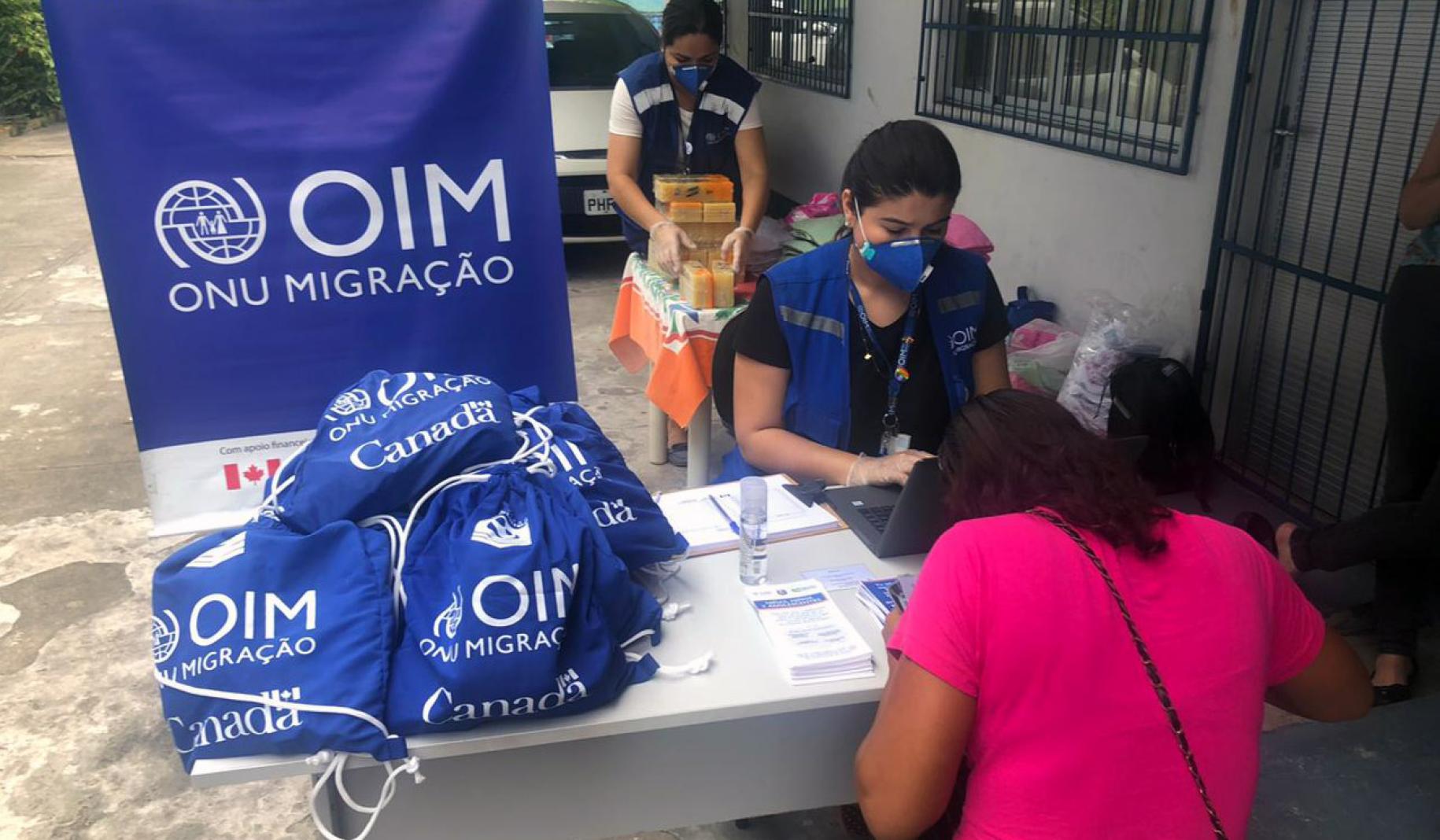 IOM staff at a distribution facility sit with a recipient of a hygiene kit. 