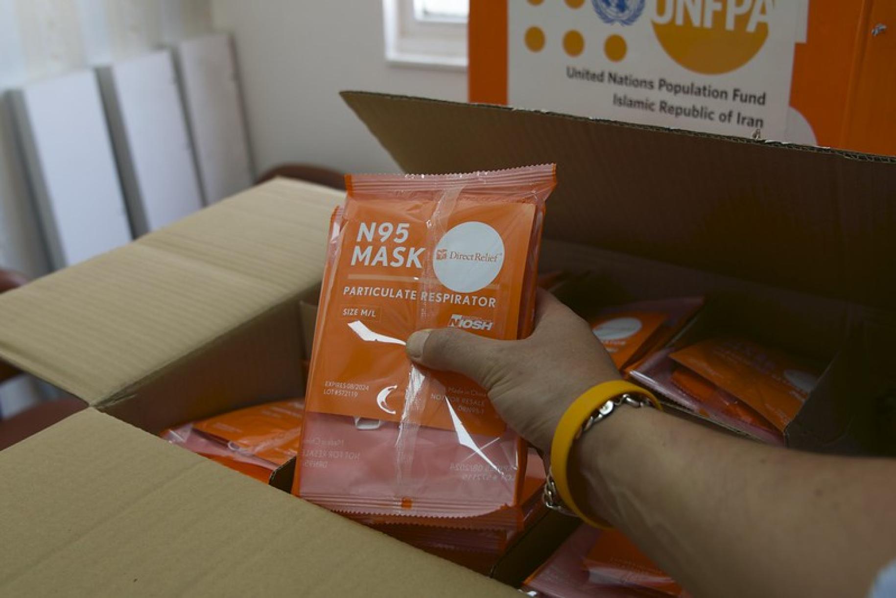 Una mano sostiene un paquete de EPP sobre una caja donada por el UNFPA.