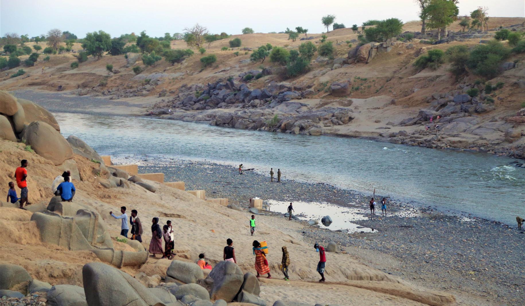 The photo shows refugees walking across an area of water and up a large hill.