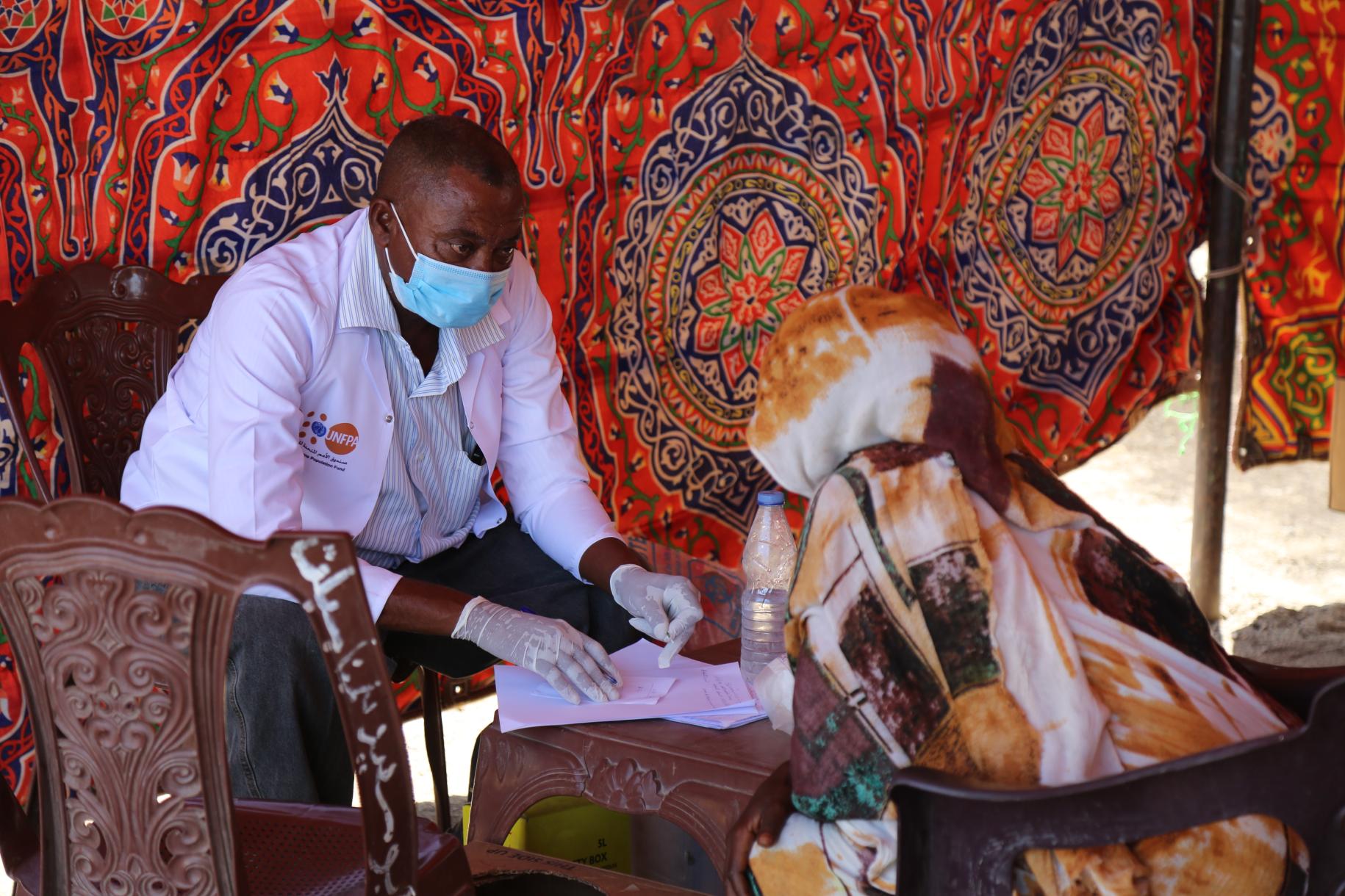 A healthcare professional sits with a patient in a tent at the camp.