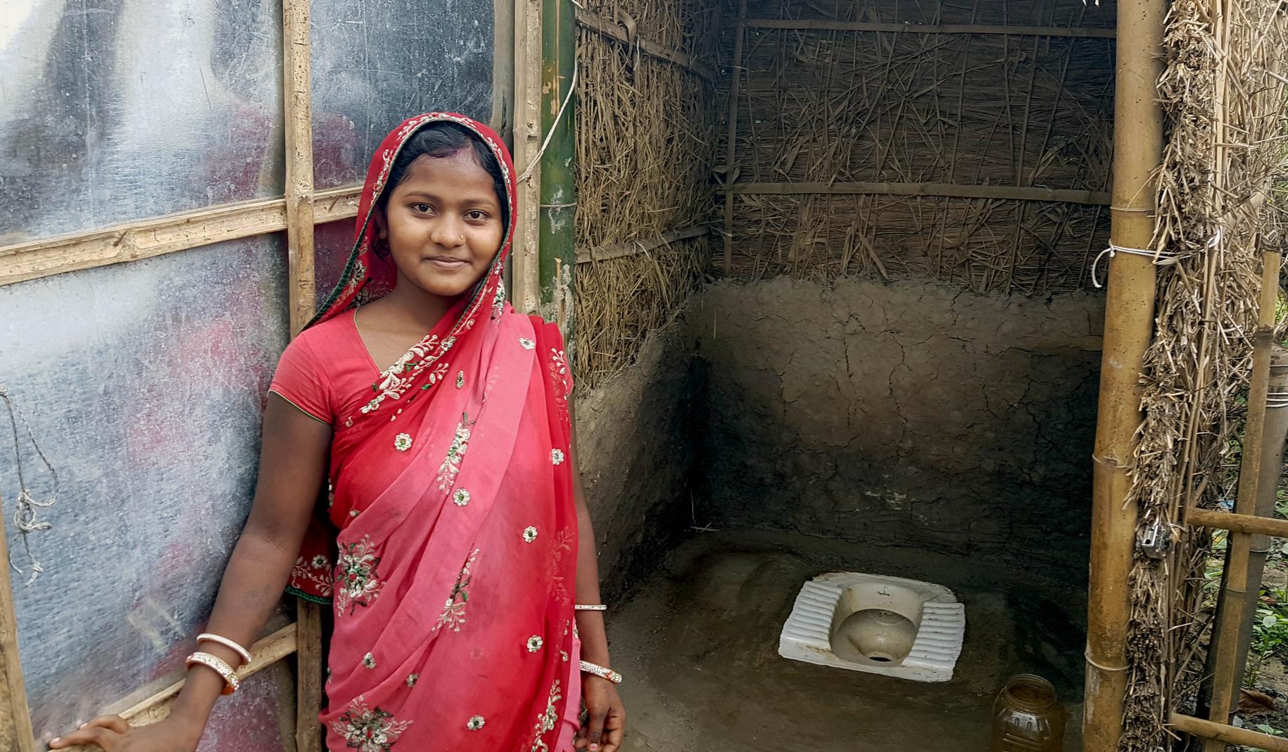 Una joven sonríe frente a un aseo en Belbari.