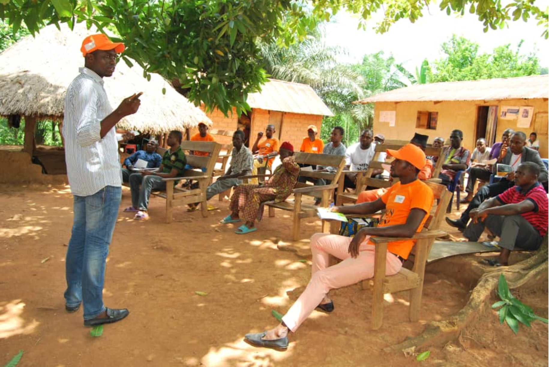 Clement stands in front of a group of men seated as he presents to them issues related to gender-based violence. 