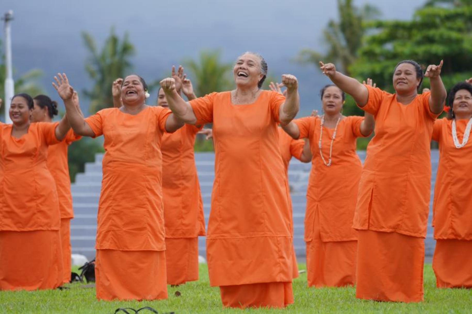 Women all dressed in orange perform at a gender-based violence event outside.