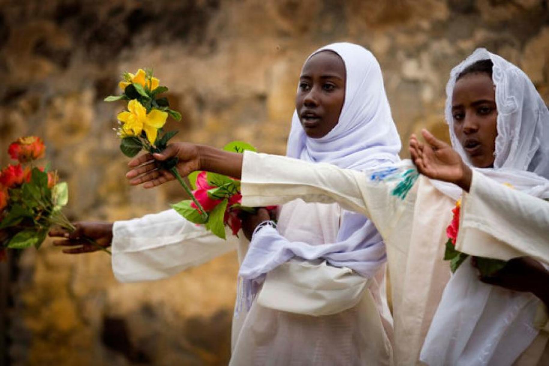 Adolescent girls are shown extending out their hands with flowers.