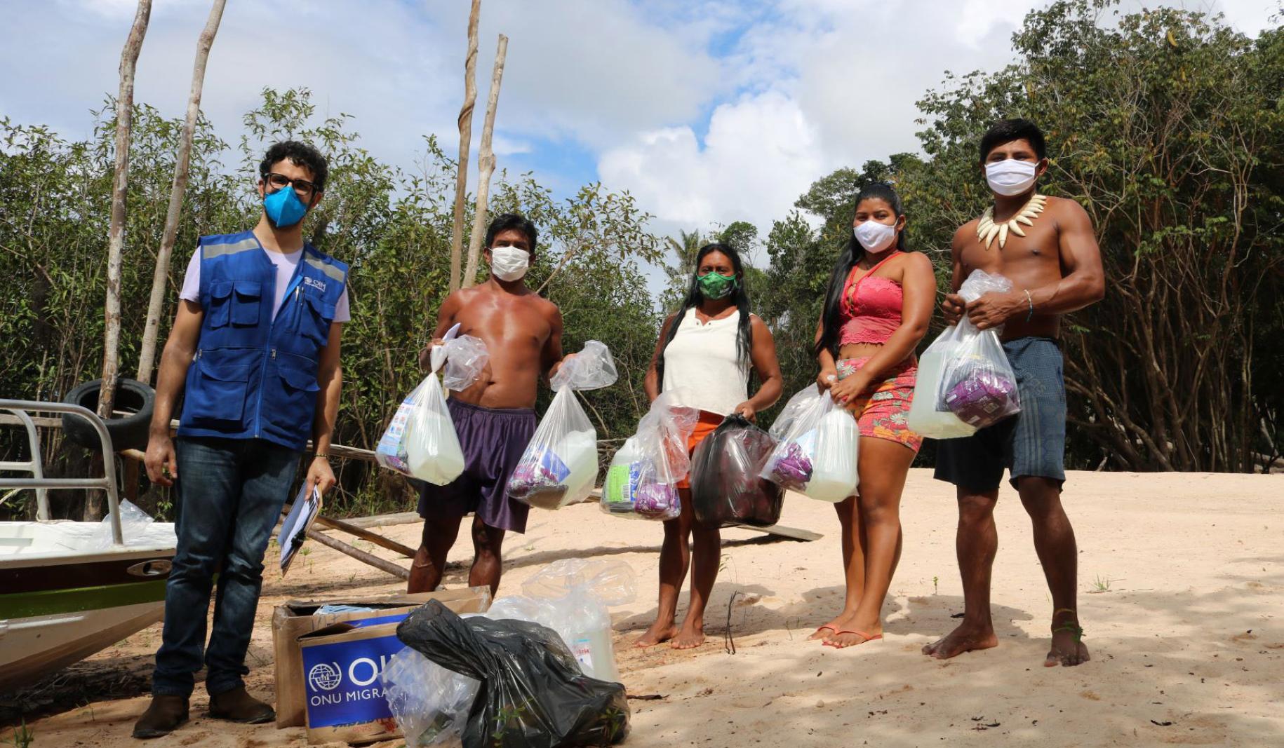 IOM staff member stands socially distanced wearing a face mask from an indigenous family after they receive supplies.