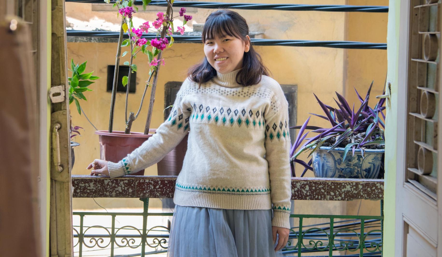 Tu Thanh Thuy se encuentra orgullosa en un porche junto a una orquídea de color magenta y plantas de color lila.