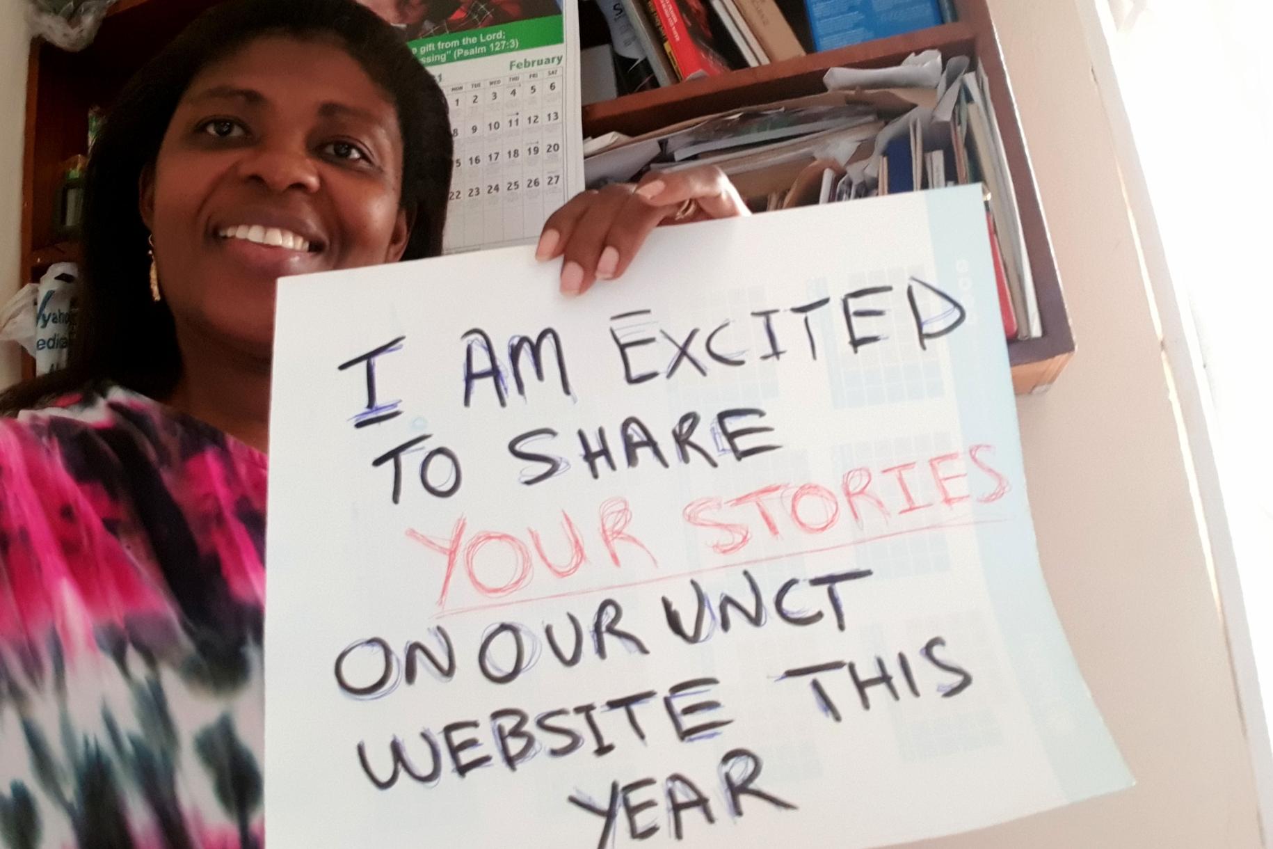Una mujer con una sonrisa, llena de orgullo, sostiene un letrero que indica que este año está emocionada de compartir más historias de personas del país en el sitio web del equipo de las Naciones Unidas en Ghana.