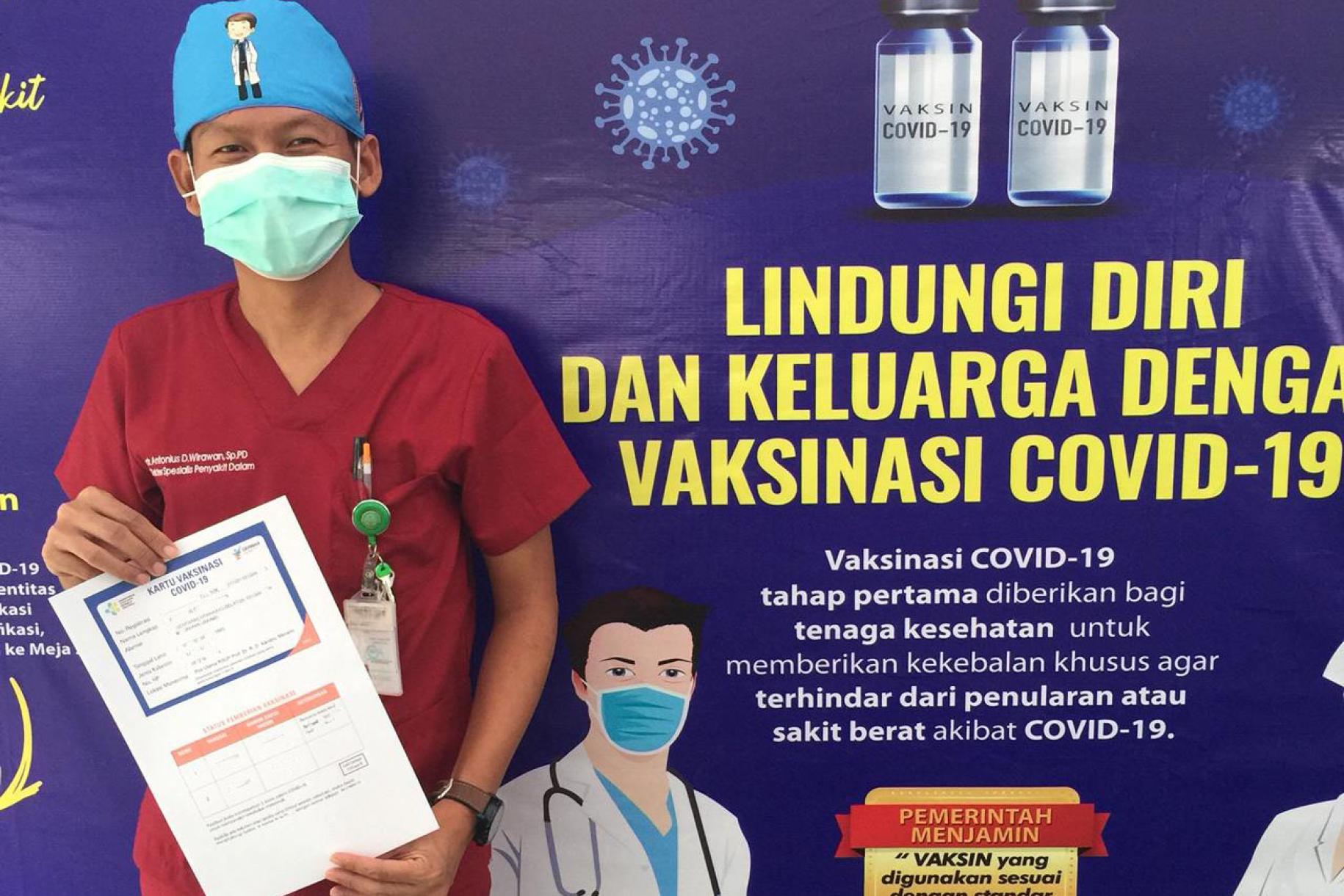 El Dr. Antonius Irawan se para frente a un cartel de vacunación COVID-19 con su certificado de vacunación COVID-19 después de recibir su primera dosis de la vacuna COVID-19 en el Hospital General del Distrito Dr. Kandou en la ciudad de Manado, provincia de Sulawesi del Norte