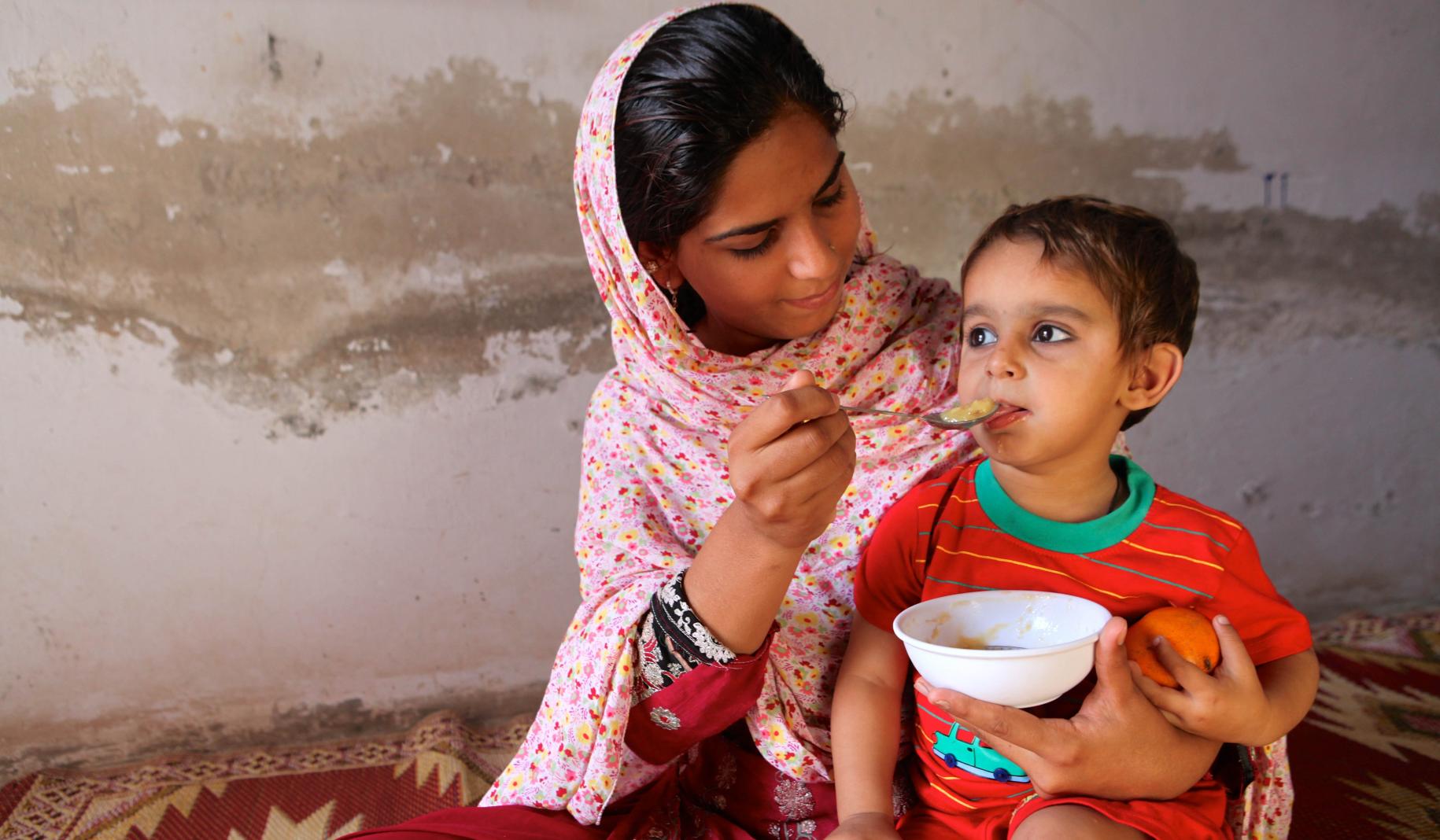 Una mujer joven sostiene a un niño en su regazo mientras lo alimenta.