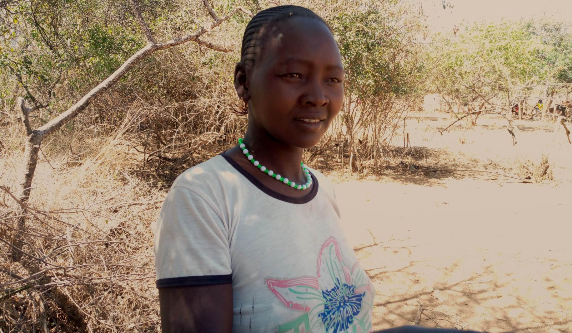 مارغريت تشيبوتيلتل، ناشطة في أوغندا تقف في الخارج بجانب شجرة وهي تحدق بعيدًا من الكاميرا.