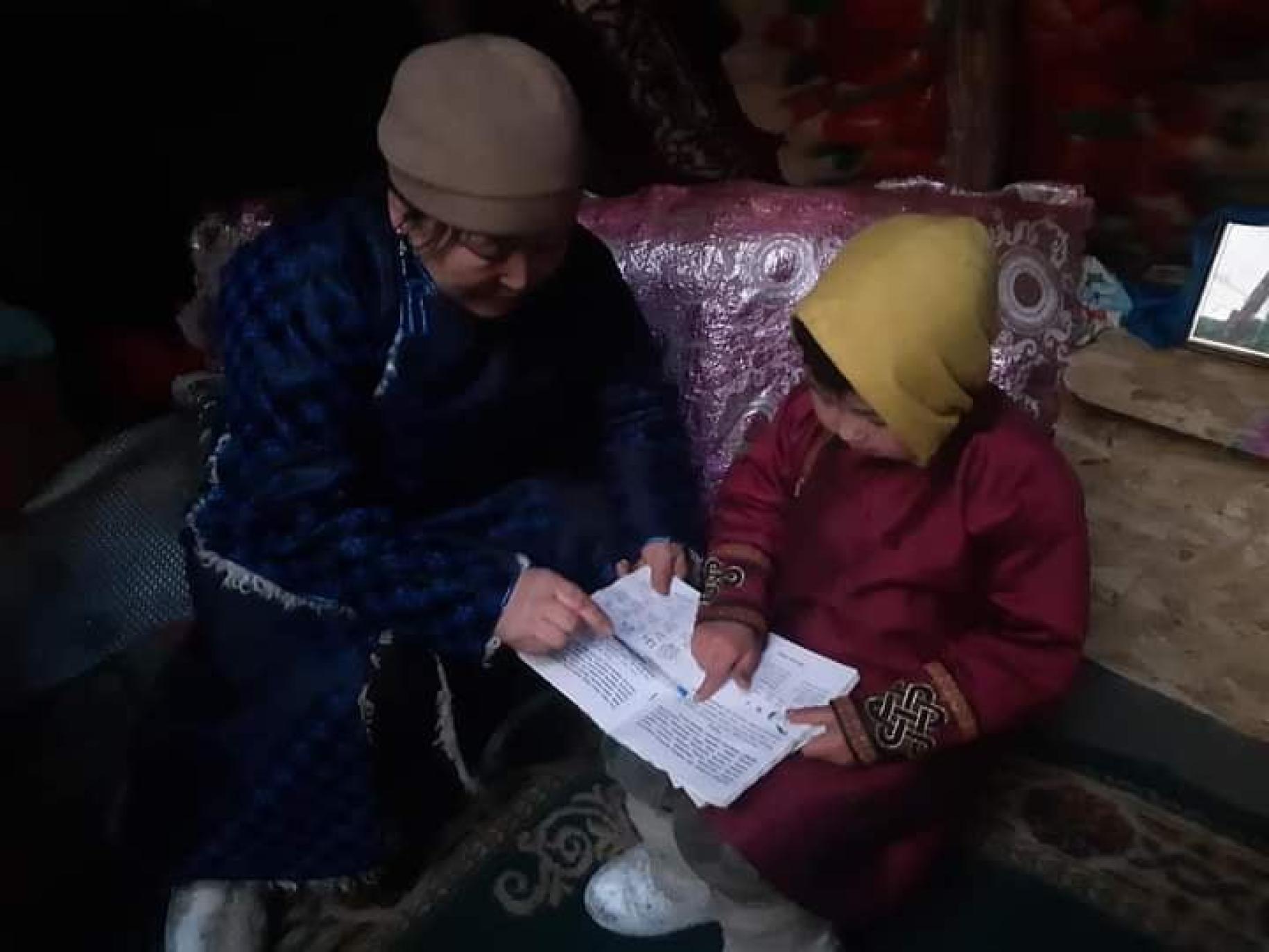 A woman dressed in blue shows a child dressed in red from a piece of paper. 