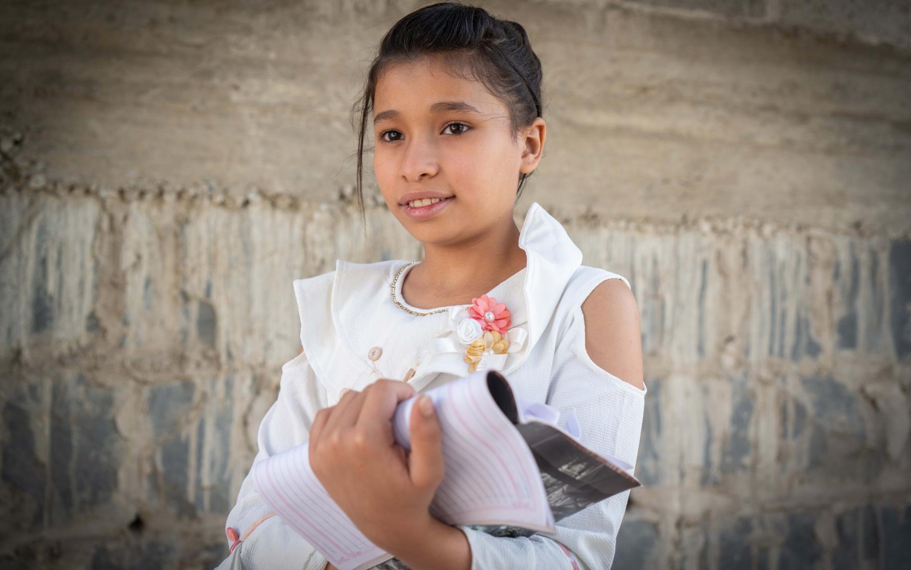 12-year-old Amina looks off the camera as she proudly holds her notebook.