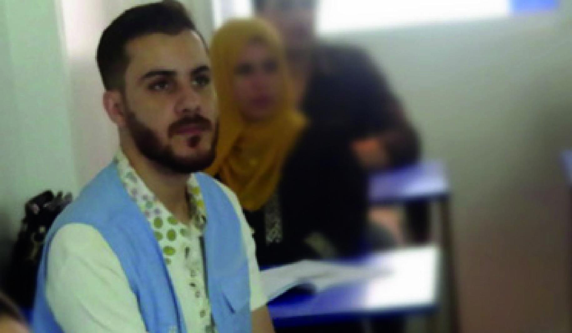 Mohammad está sentando en su puesto en un salón de clases, mientras escucha con atención a la persona que lidera la lección.