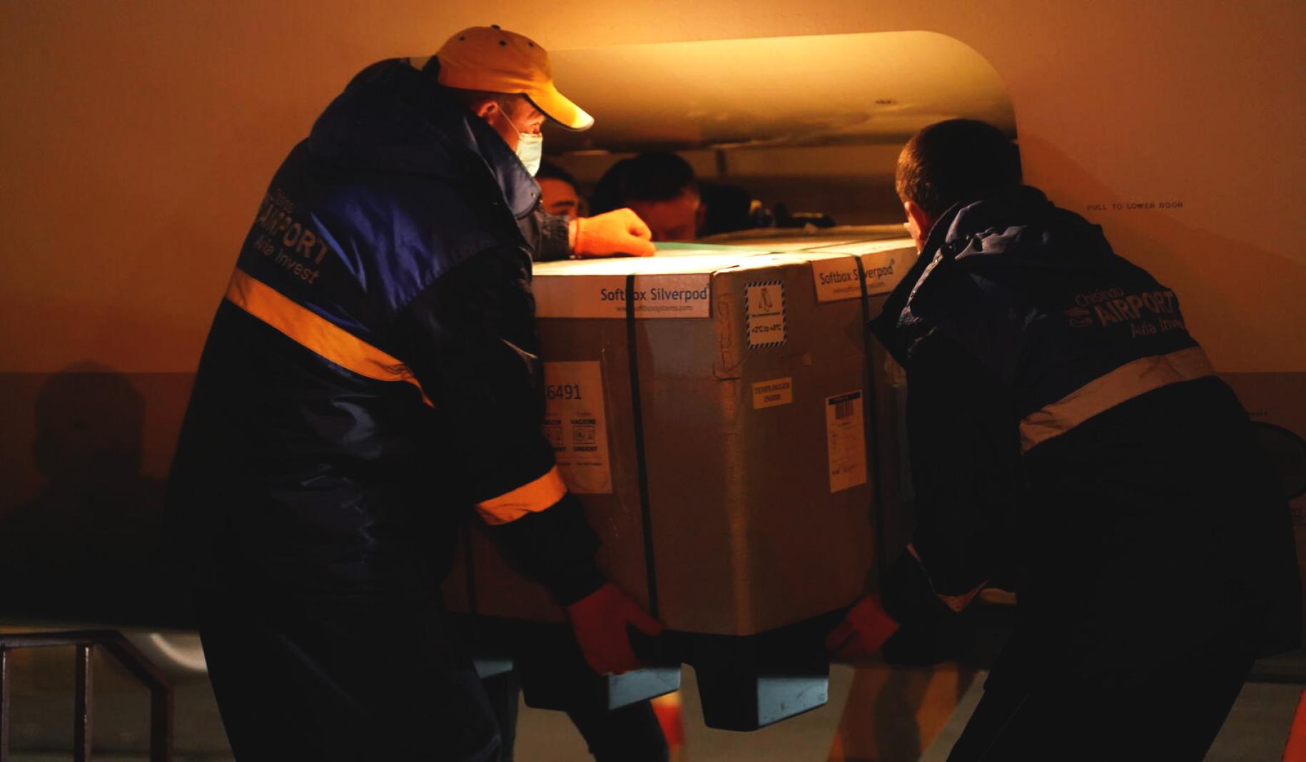Two airport employees unload a crate of vaccines from the plane's cargo space.