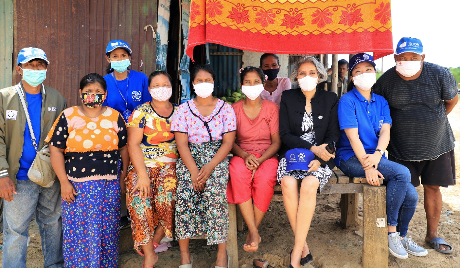Plusieurs femmes et hommes portant un masque de protection respiratoire, dont la Coordonnatrice résidente de l’ONU en Thaïlande, Gita Sabharwal, sont assis côte à côte sur le bord d’une grand table en bois, en extérieur, et regardent en direction de l’objectif.