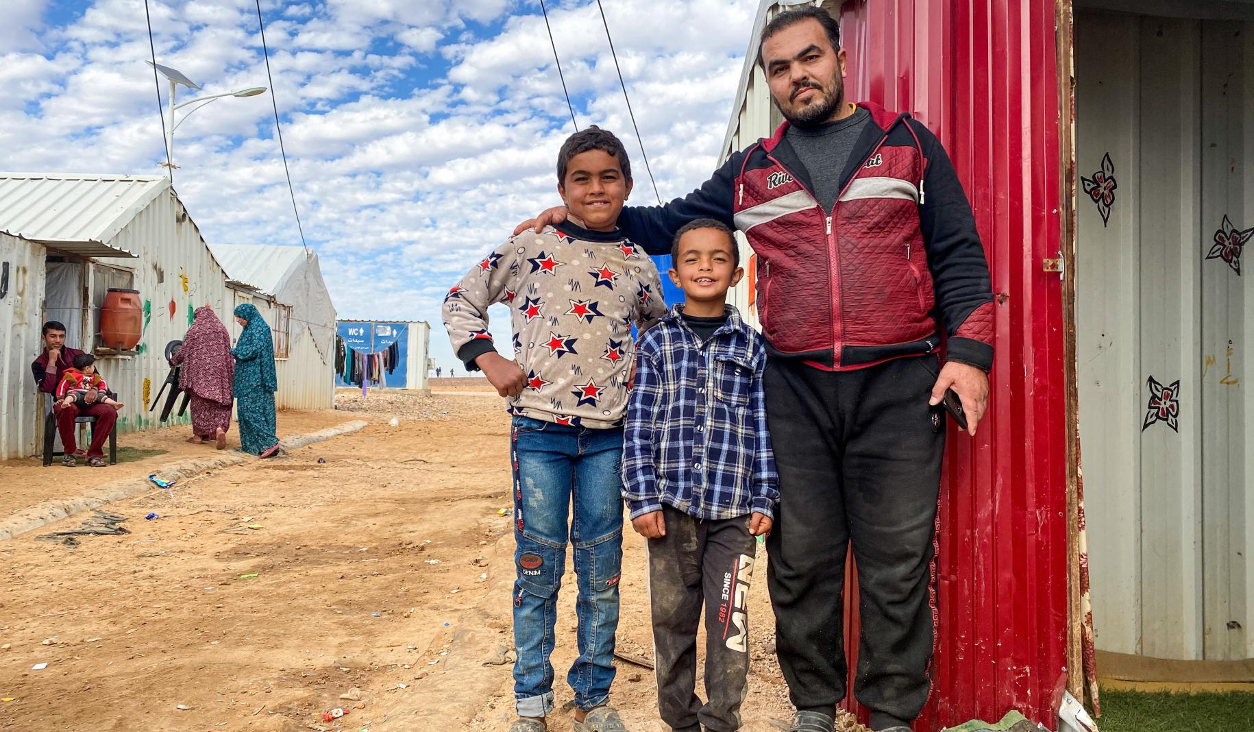 Ahmad coloca con orgullo sus brazos alrededor de sus dos hijos pequeños mientras están fuera de su casa y posan para la cámara.