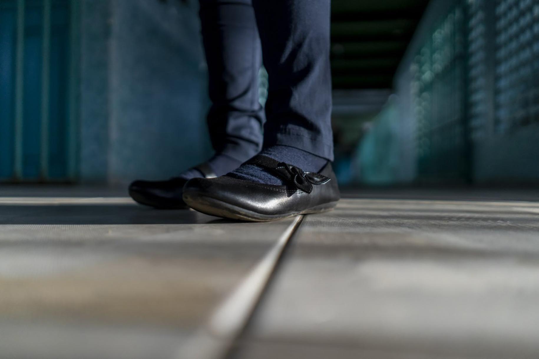 A close up image of a girl's black shoes and blue school uniform up to the knees. 