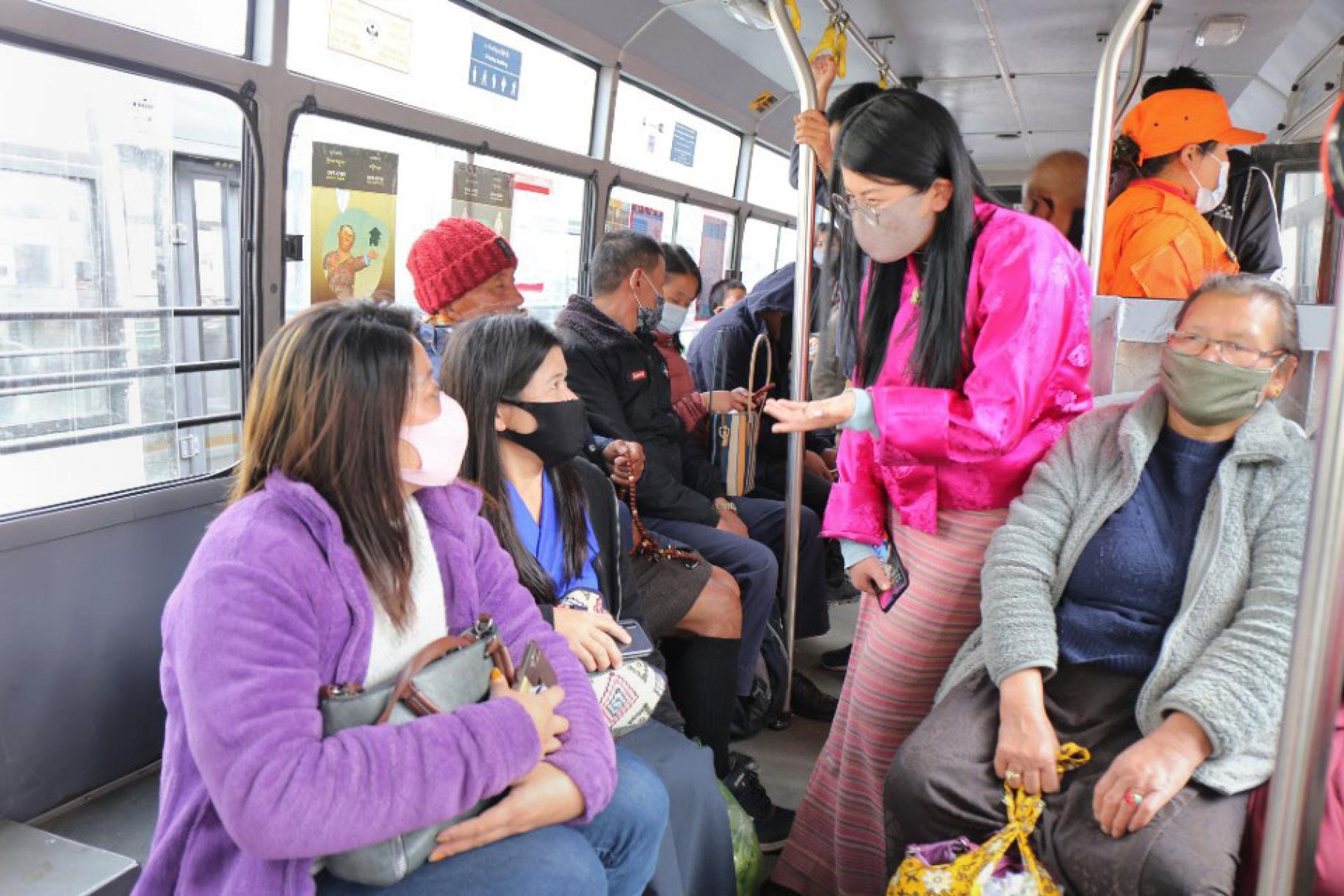 Several people in bright colors wearing masks ride on a bus.