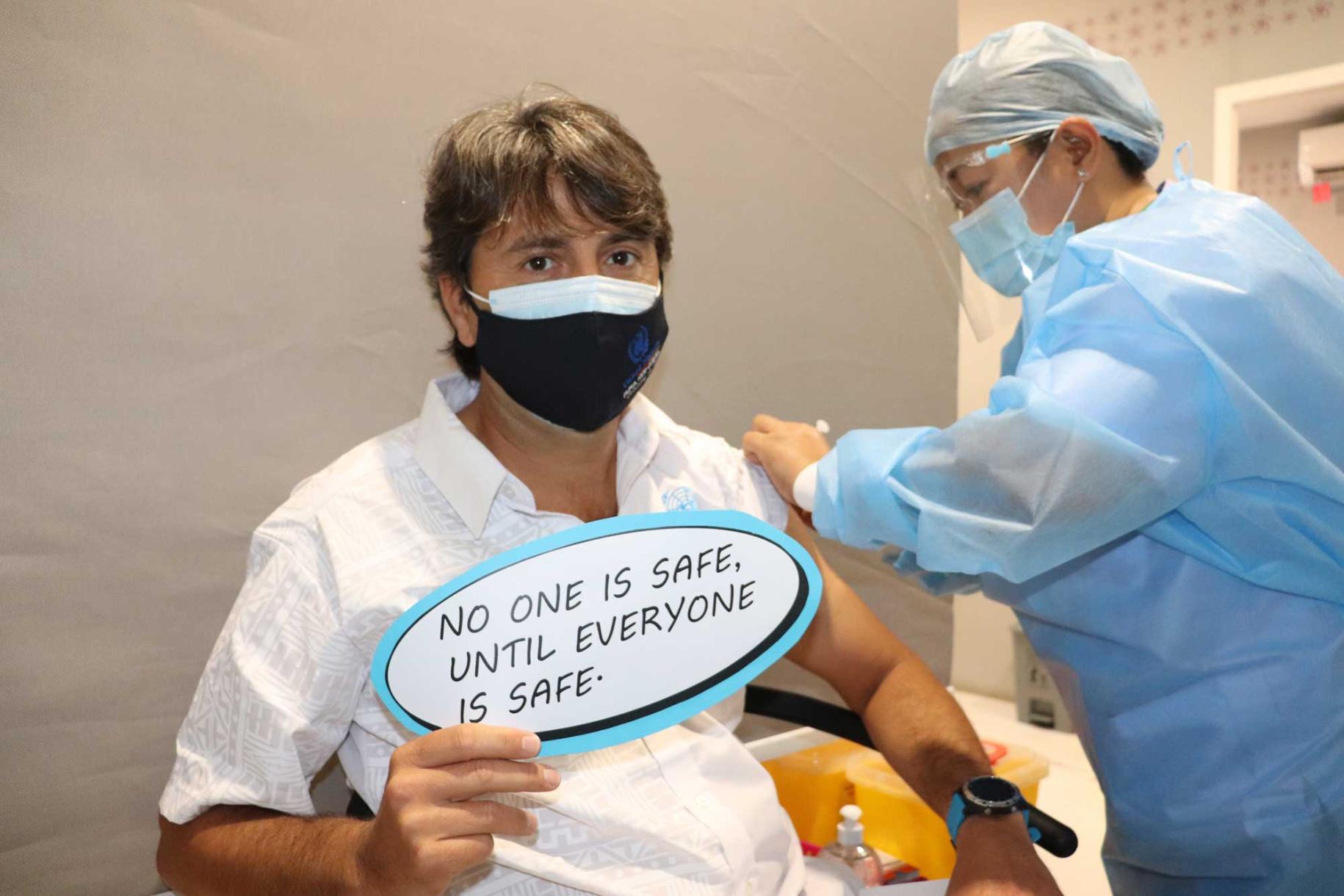 Le Coordonnateur résident de l'ONU en Papouasie-Nouvelle-Guinée se fait administrer un vaccin anti-COVID-19 en affichant un panneau indiquant "No one is safe until everyone is safe", qui signifie en français "Personne n'est en sécurité tant que tout le monde ne l'est pas".