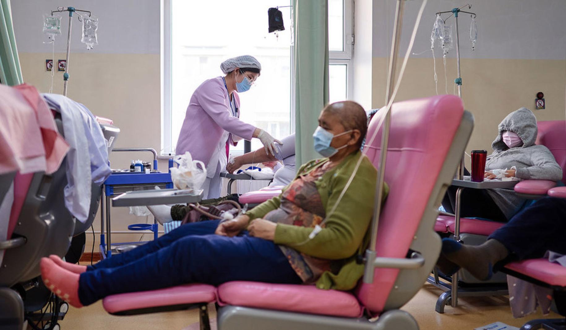 En un consultorio médico, una persona se sienta en una silla rosa y recibe un medicamento por vía intravenosa.