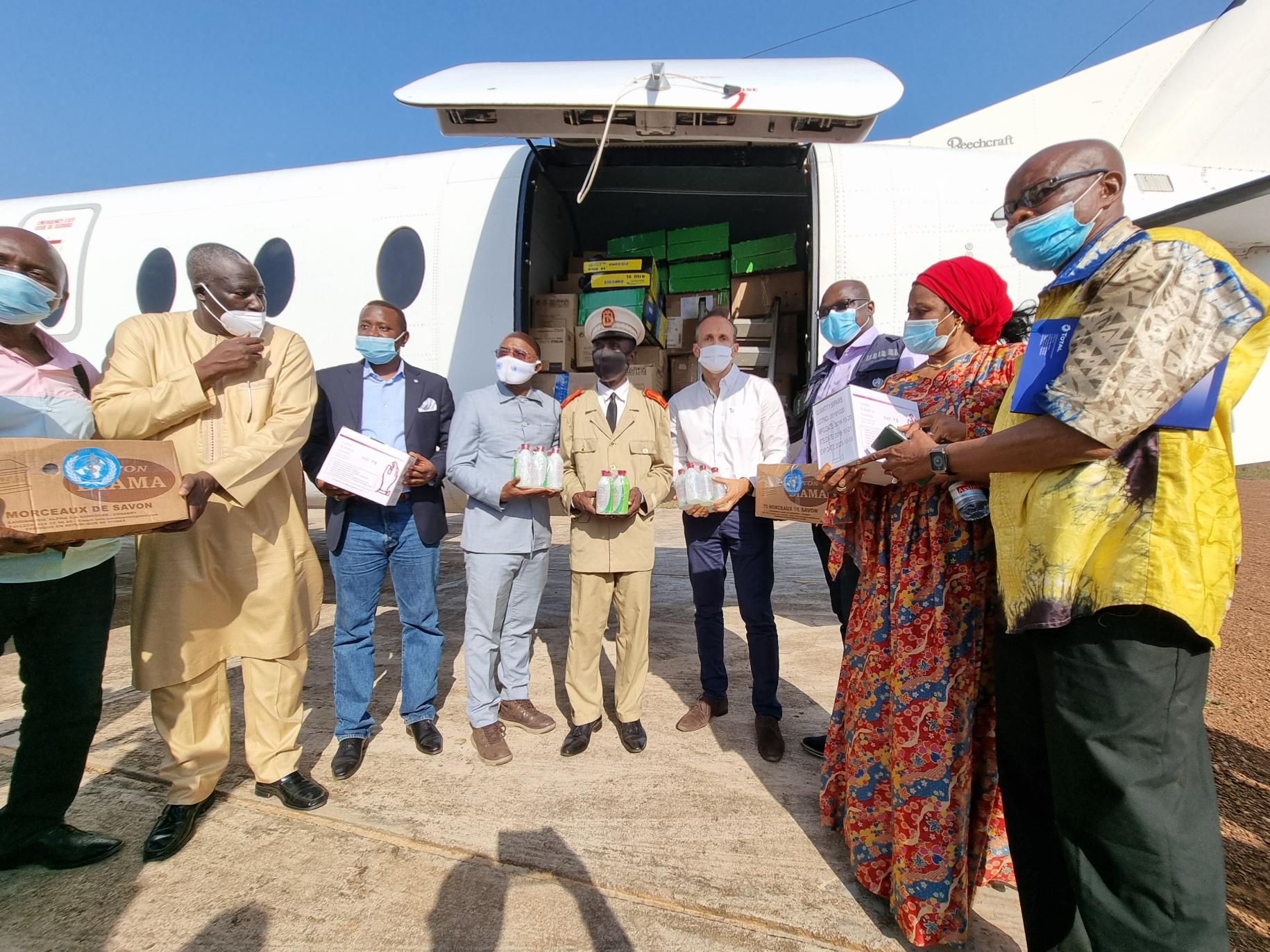 Plusieurs hommes et femmes portant des masques de protection, dont Vincent Martin, le Coordonnateur résident de l’ONU en Guinée, de tiennent debout, des fournitures dans les mains, devant la porte ouverte d'un avion.