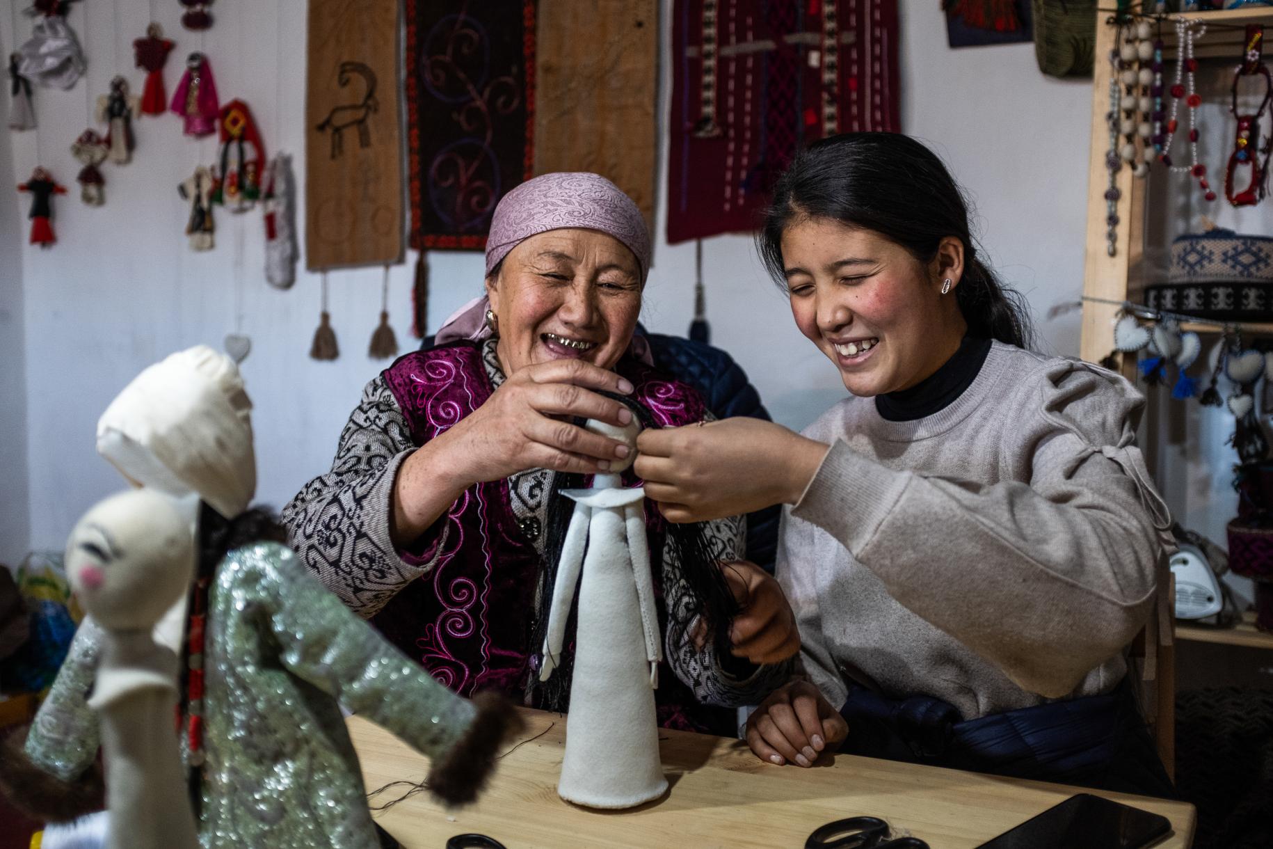 Two women smile while they put together a doll. 