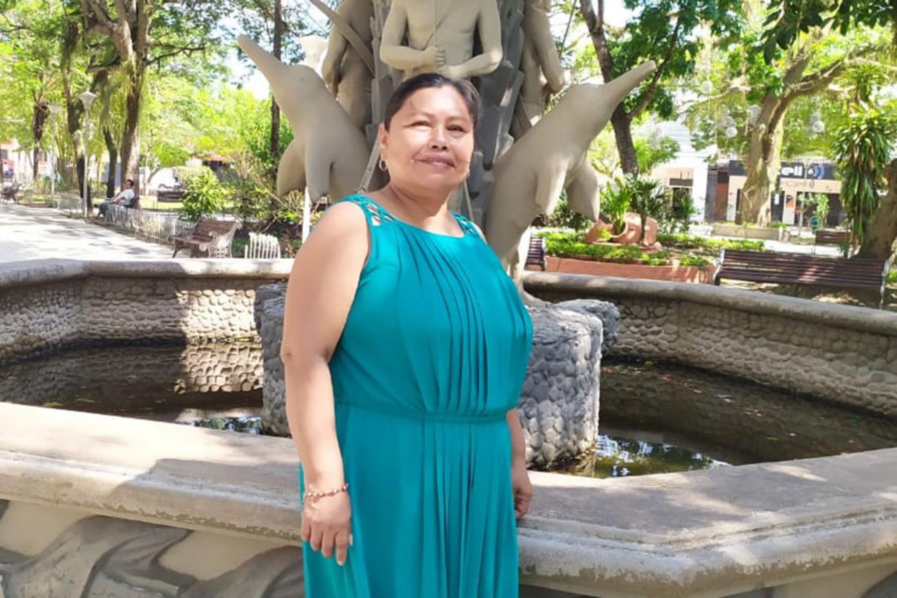 A woman in a teal dress stands in front of a fountain. 