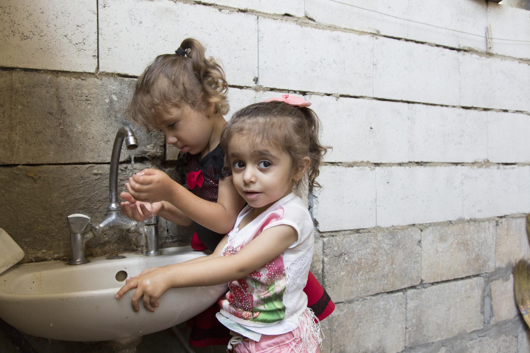 Two little girls washing their hands in an outdoor sink.