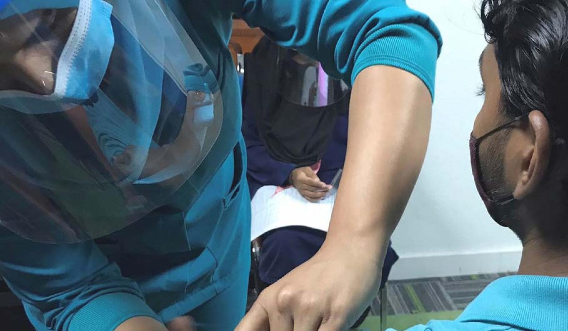 一个戴口罩和面罩的人给一个戴口罩和穿茶色衬衫的人注射疫苗。