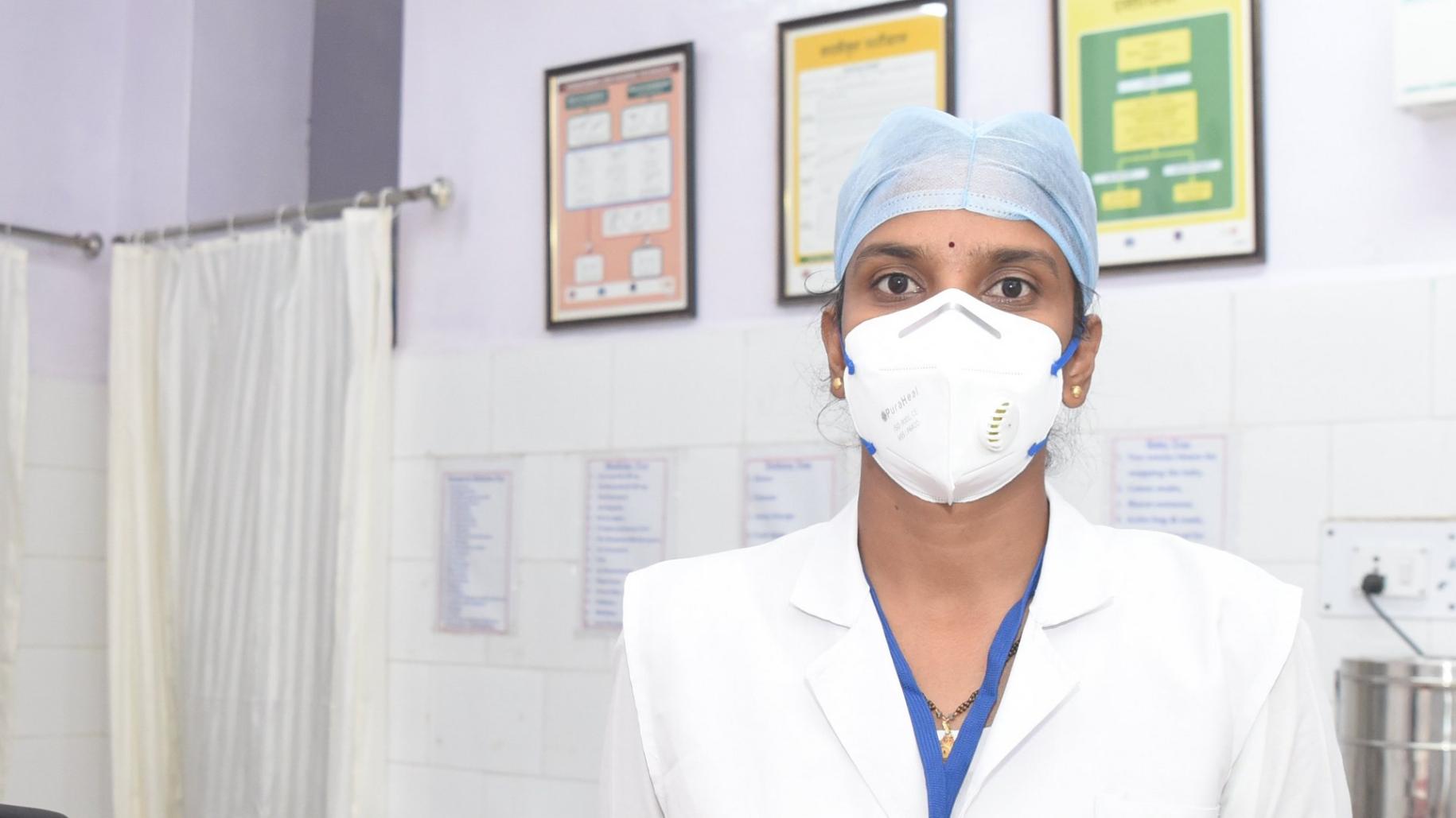 Une infirmière portant un masque de protection respiratoire et une charlotte est prise en photo dans les locaux d’un établissement de soins indien.