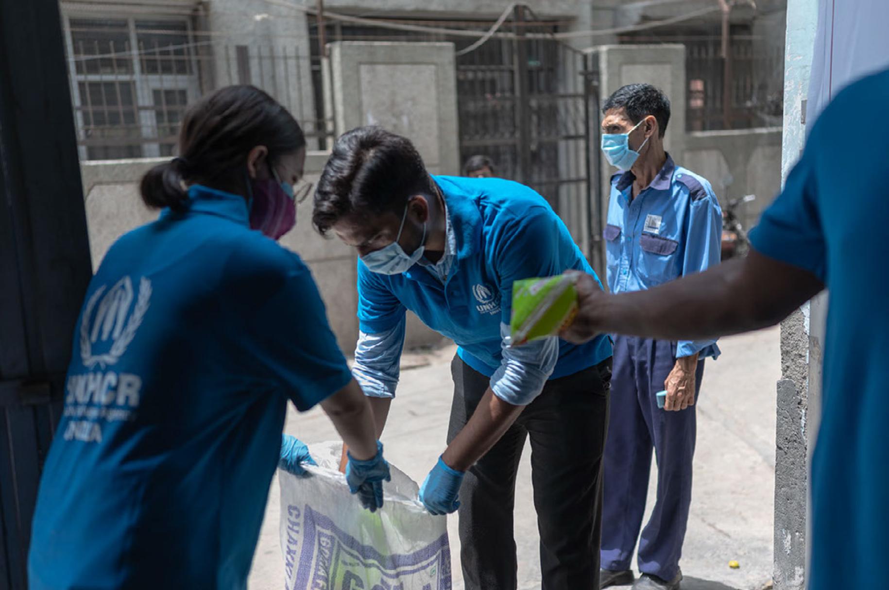 En Inde, des membres du personnel du HCR portant chacun le polo de l’Organisation et un masque de protection respiratoire s’affairent autour d’un grand sac en plastique.