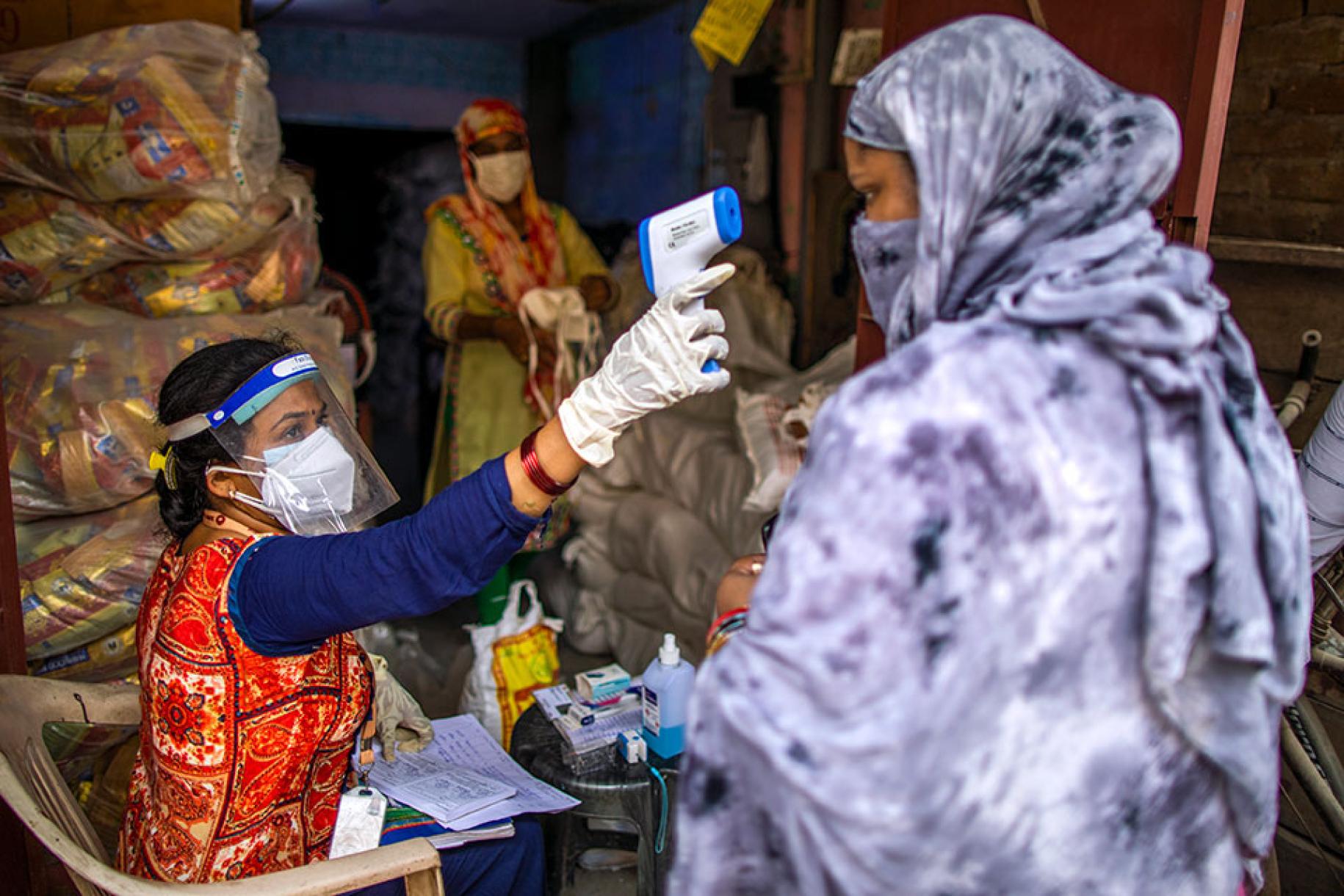 A New Delhi, en Inde, une travailleuse communautaire de l’association SEWA portant un masque de protection respiratoire contrôle la température corporelle d’une femme entièrement voilée à l’aide d’un thermomètre sans contact.