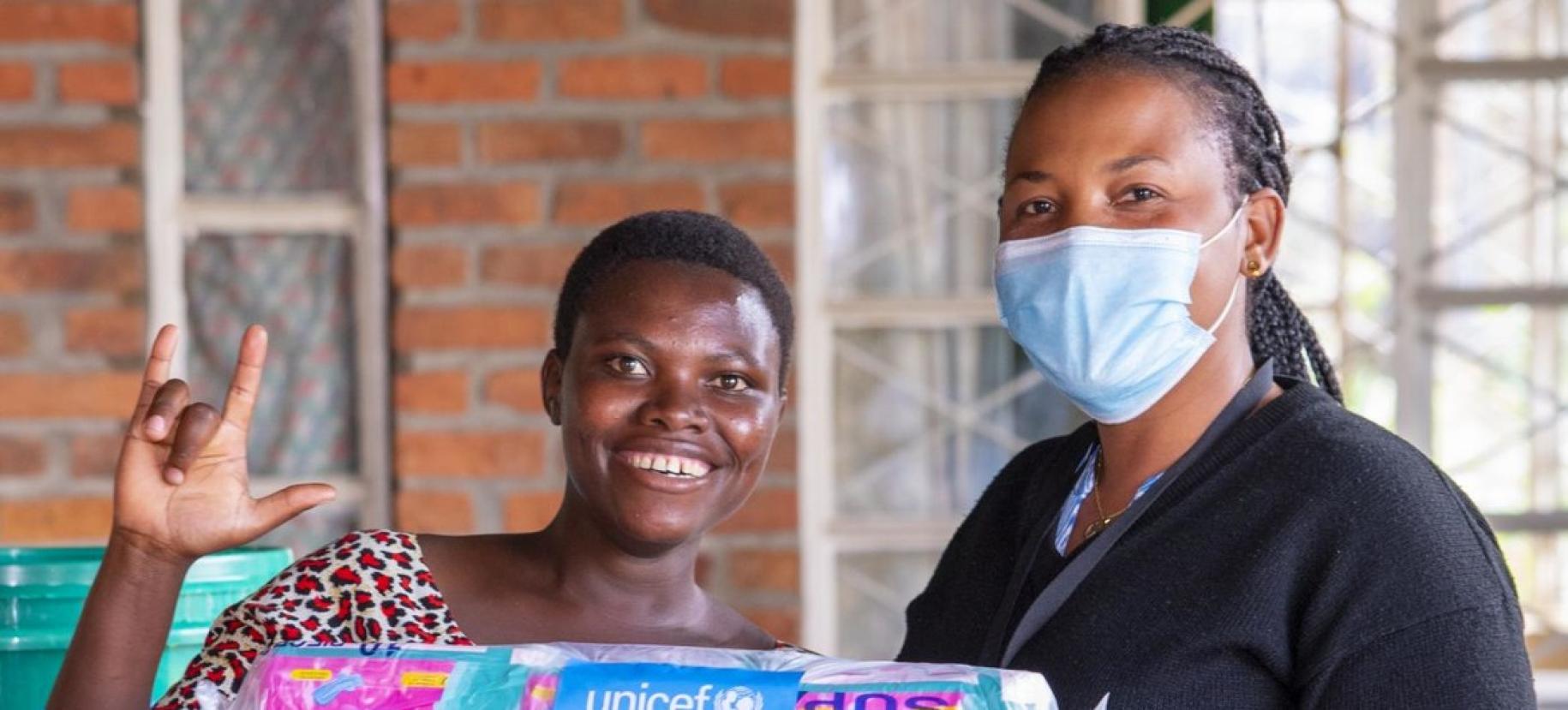 Deux femmes africaines, dont une portant un masque de protection respiratoire, se tiennent côte à côte devant l’objectif en souriant. 