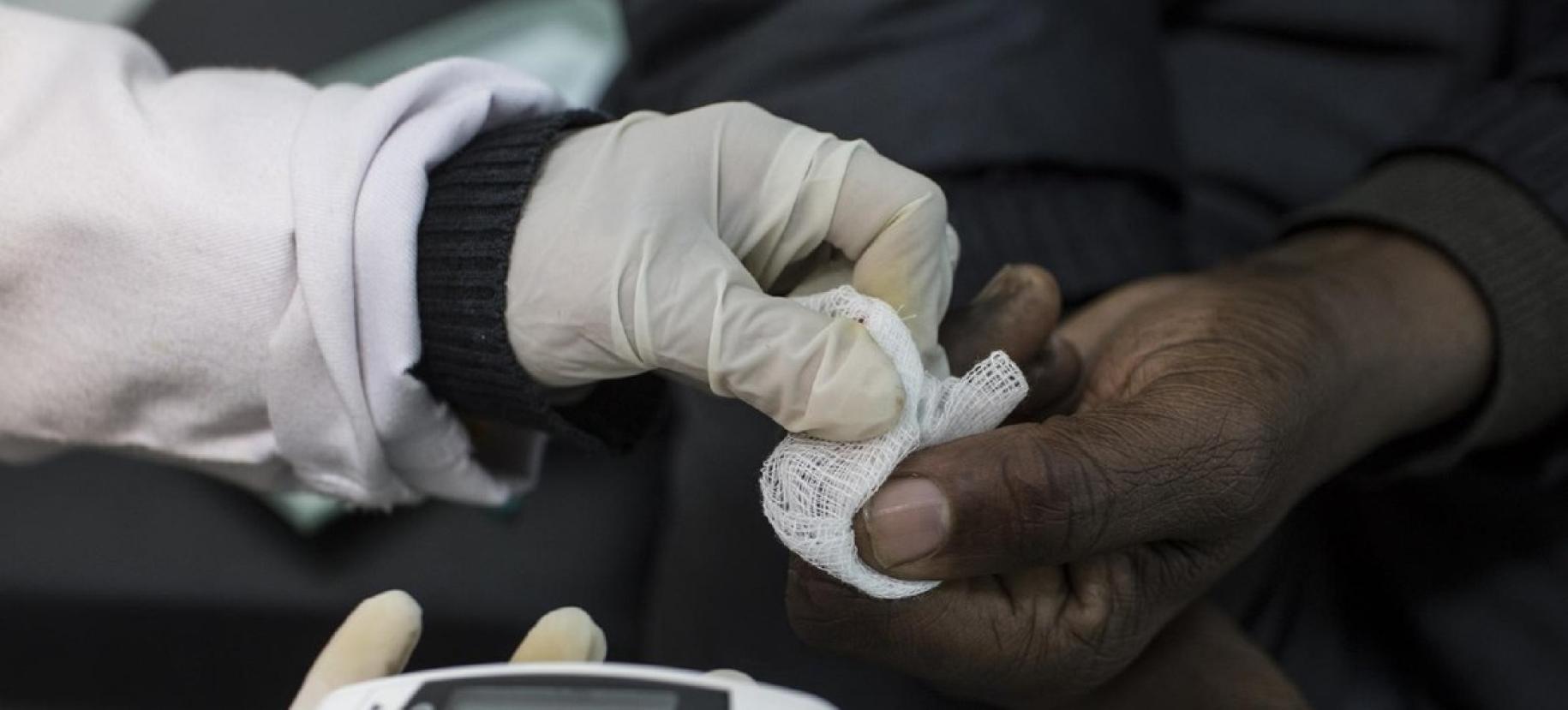 Gros plan sur la main gantée d'un professionnel de santé effectuant un test de dépistage du diabète en Afrique.