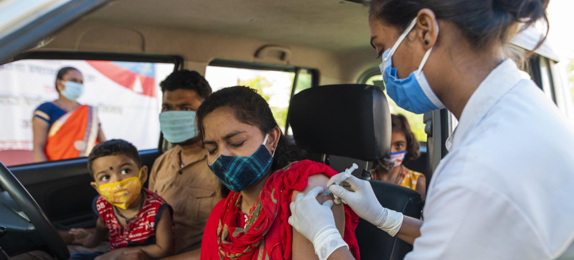 امرأة تتلقى اللقاح صد كوفيد-19 في السيارة وبجانبها رجل وطفل في حضنه.
