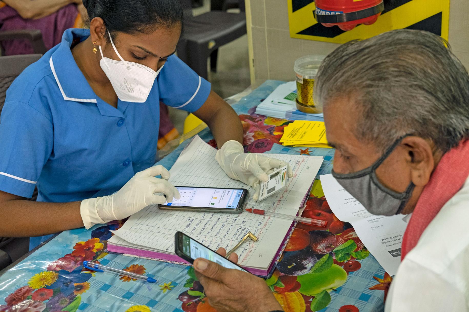 Une professionnelle de santé vêtue d’une blouse bleue consigne dans un application mobile le vaccin anti COVID-19 que l’homme assis devant elle vient de se faire administrer.