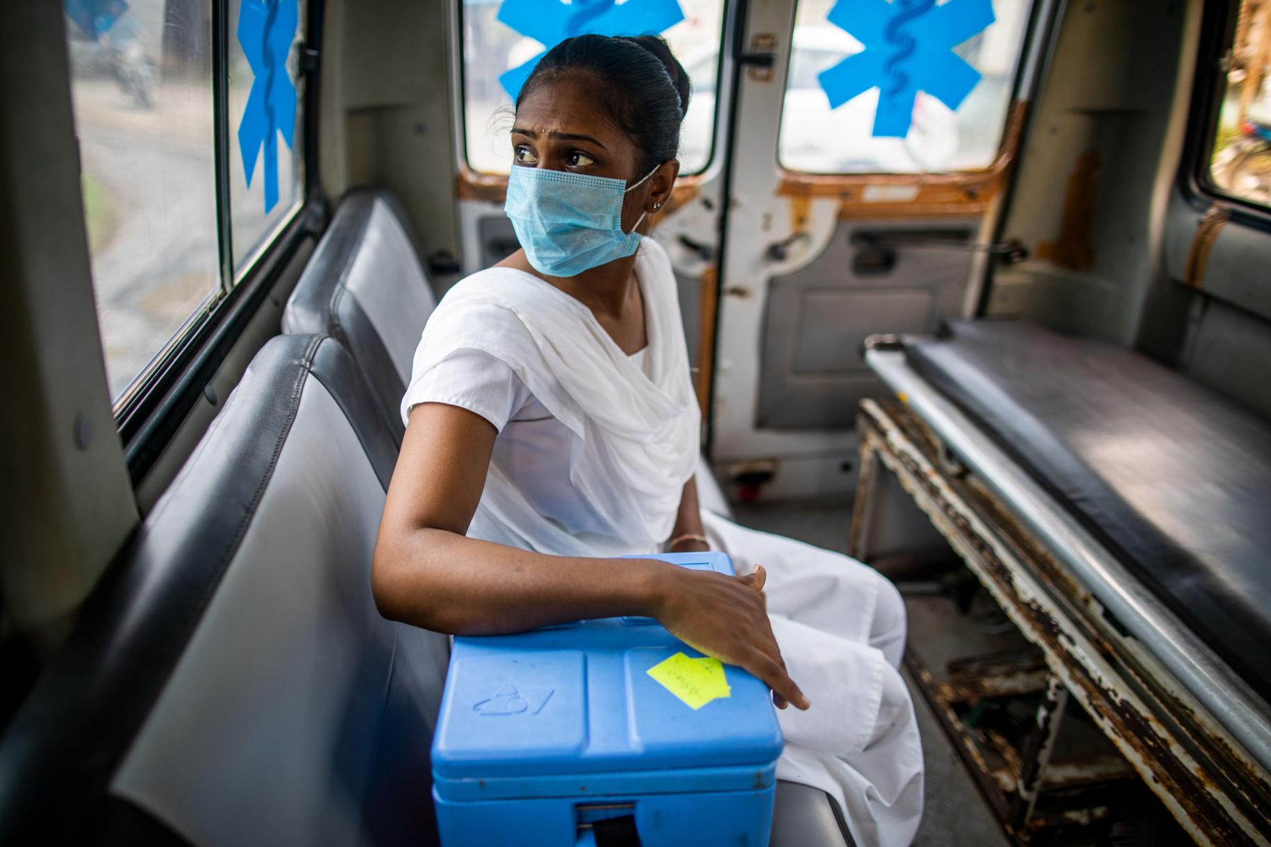 Dans l'ouest de l'Inde, une sage-femme infirmière portant un masque de protection respiratoire est assise dans une ambulance, la main posée sur une glacière contenant des vaccins anti COVID-19, et lance un regard inquiet à travers la fenêtre.