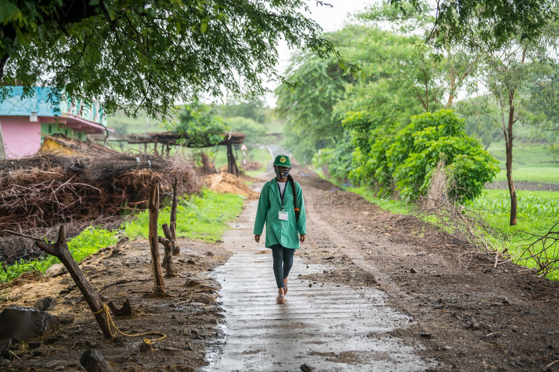 A person in a green jacket walks down a muddy road. 