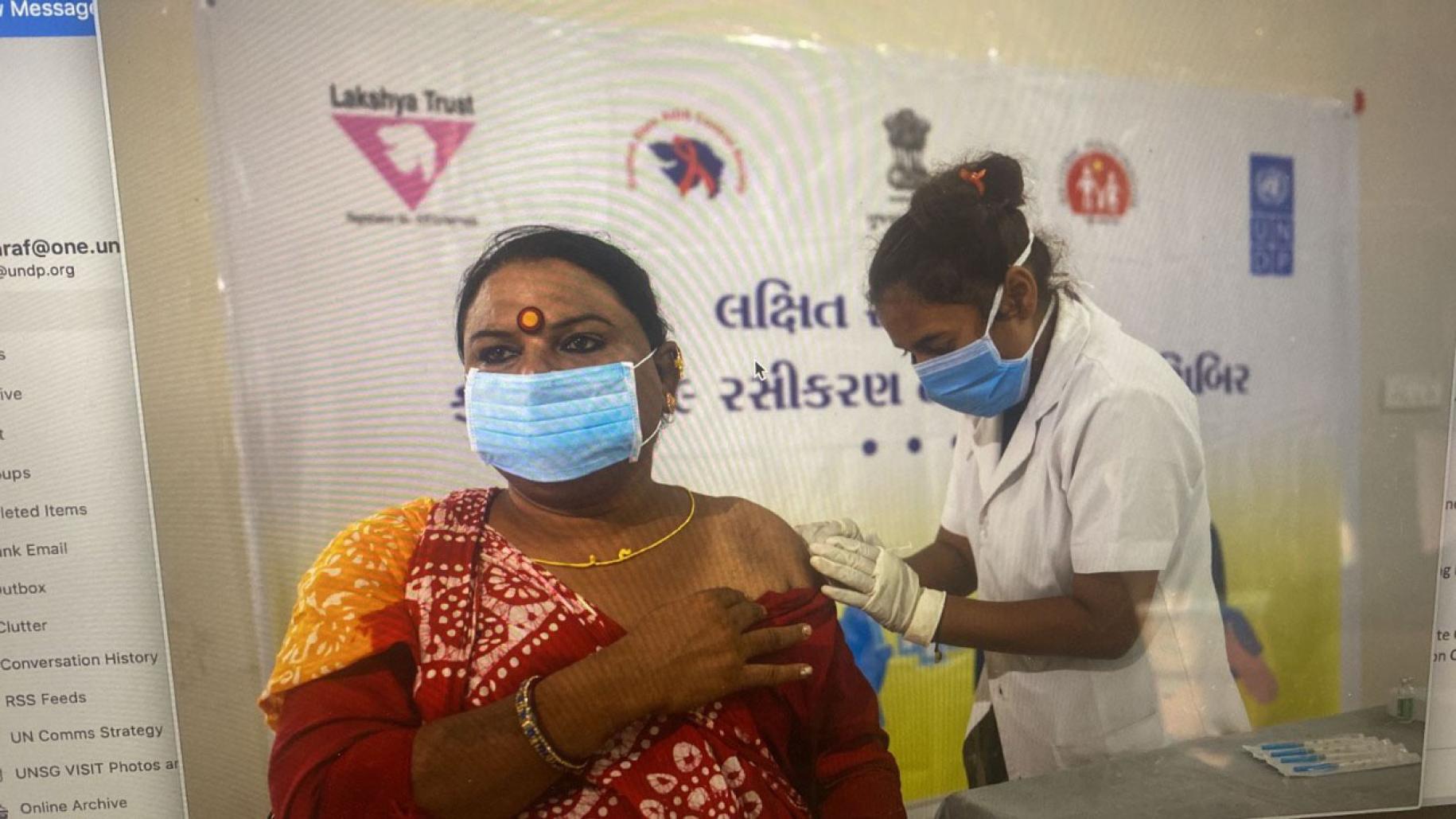 A woman in a light blue face mask receives a vaccine from a medical professional.