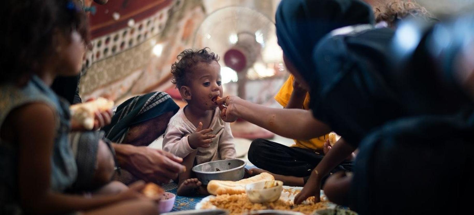 Un niño de un año come con su familia en un campamento de desplazados internos en Adén, Yemen.